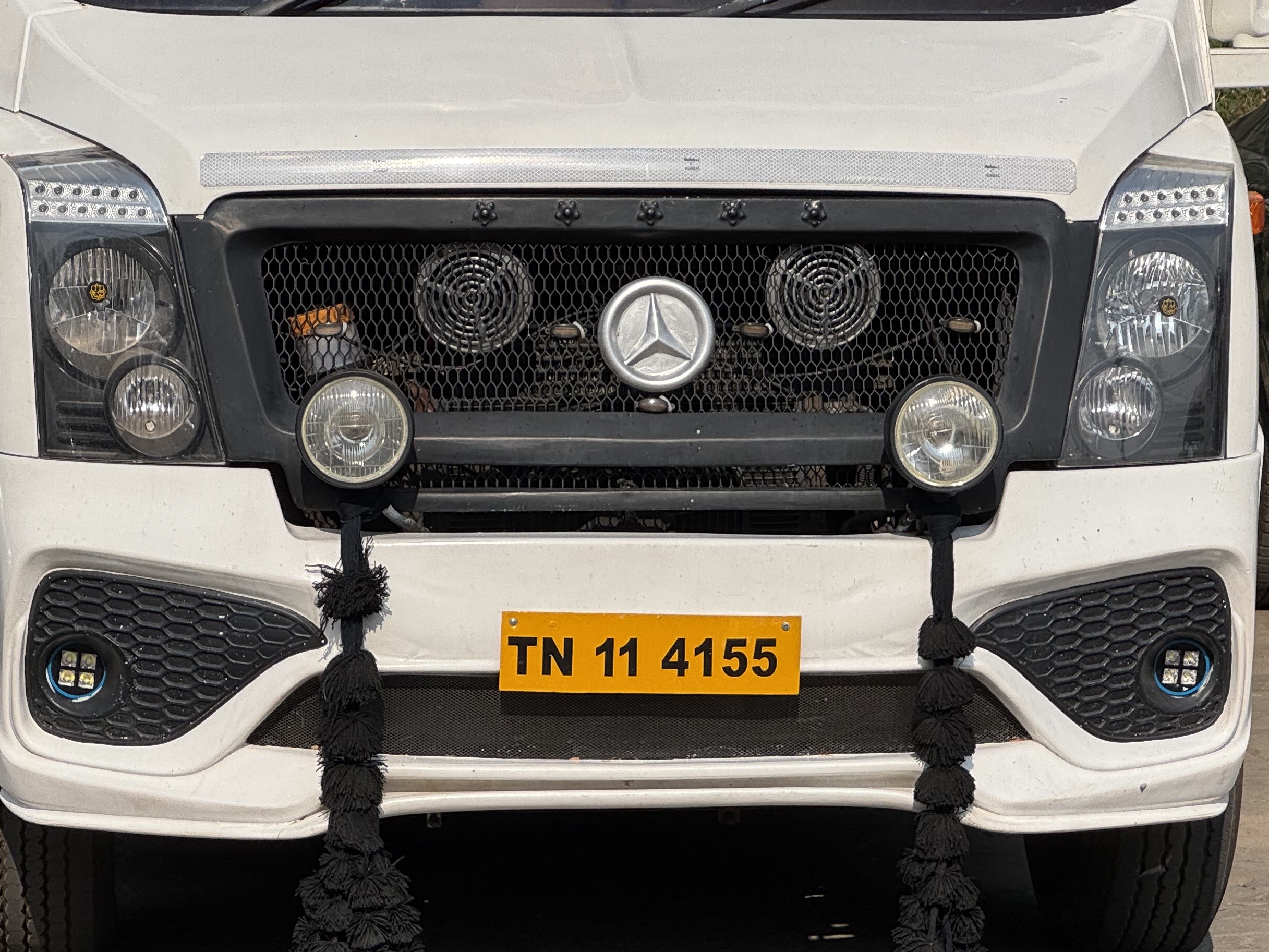 Front view of a white truck with Mercedes-Benz emblem, black honeycomb grille, round headlights, and a yellow TN 11 4155 license plate.
