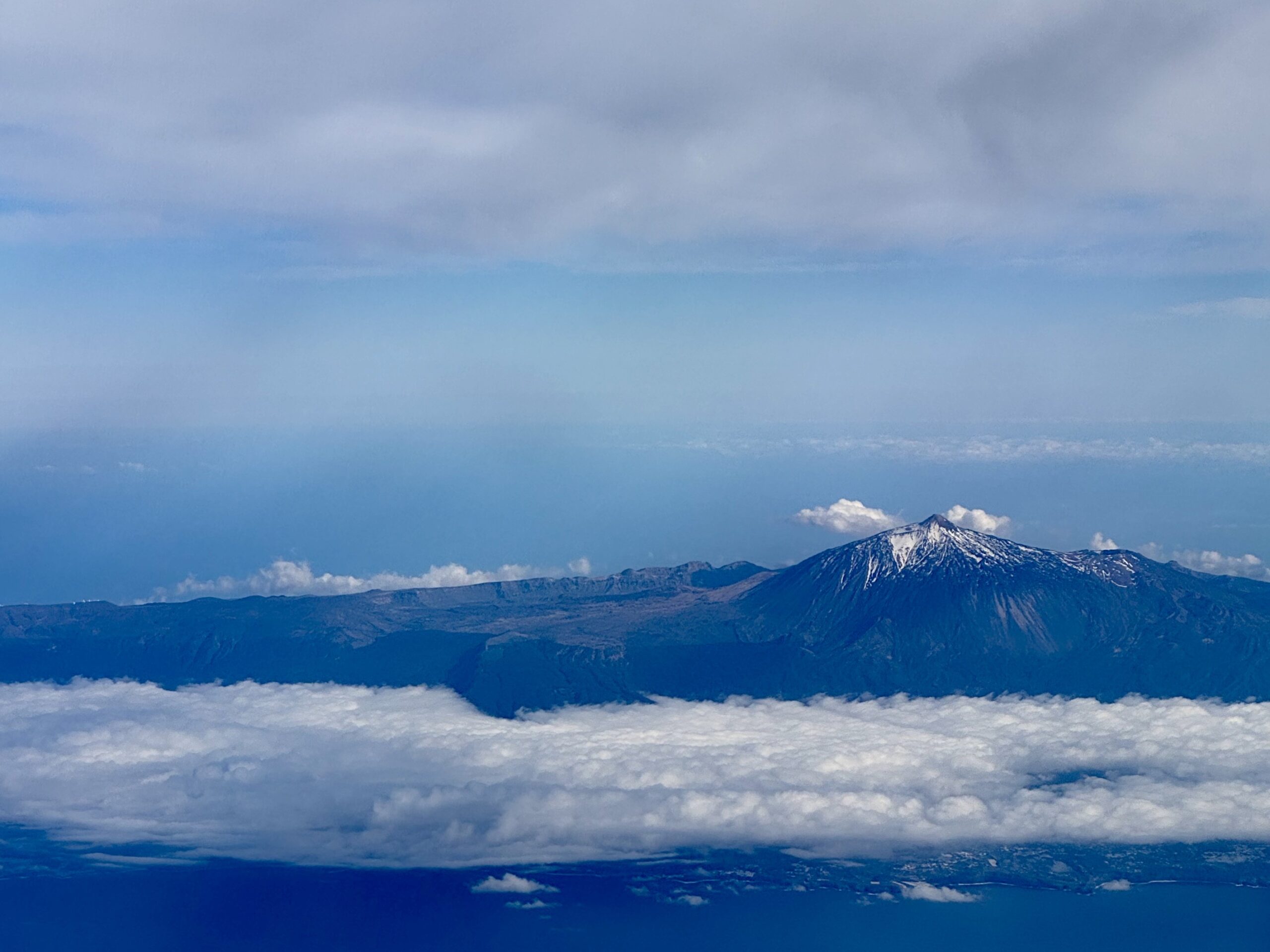 Snow-capped mountain range viewed from above the clouds under a blue sky.