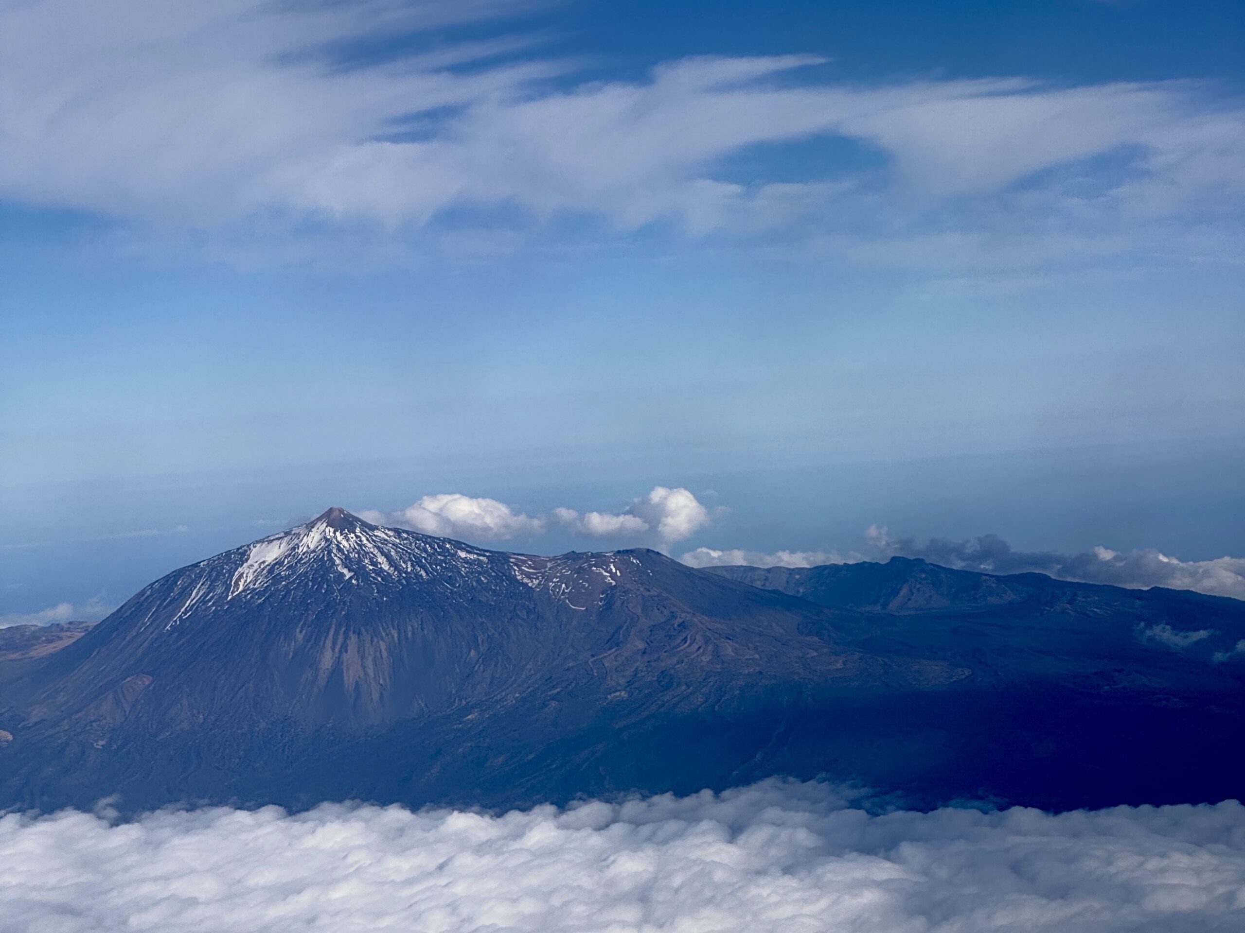 Snow-capped mountain peak rising above a sea of clouds under a clear blue sky.