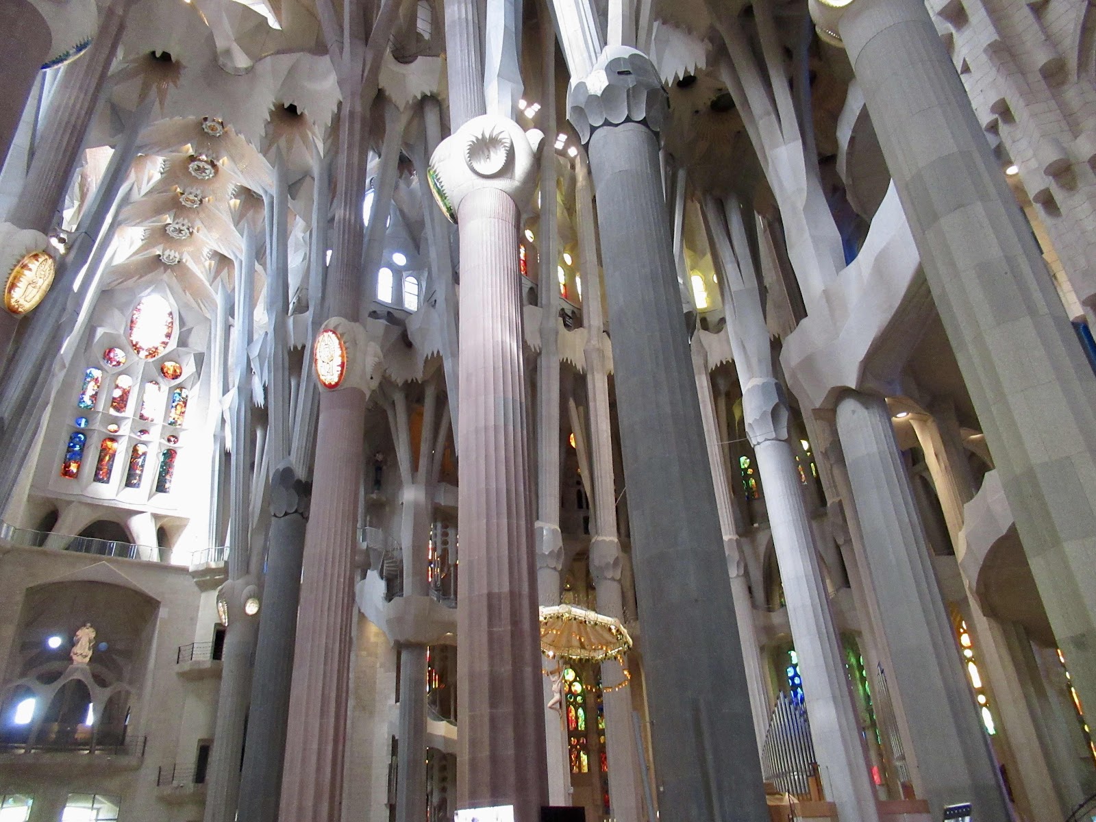 Interior of the Sagrada Família showing tall, tree-like columns and colorful stained-glass windows.