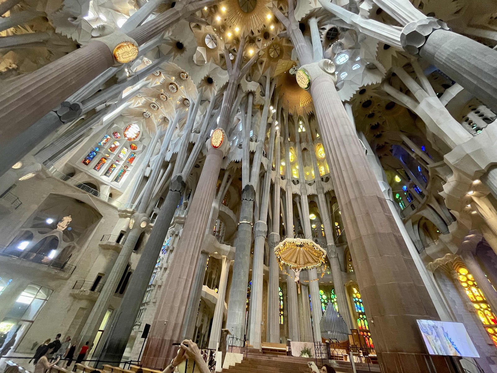 Interior of the Sagrada Família with tall tree-like columns, vaulted ceiling, and colorful stained-glass windows framing the nave.
