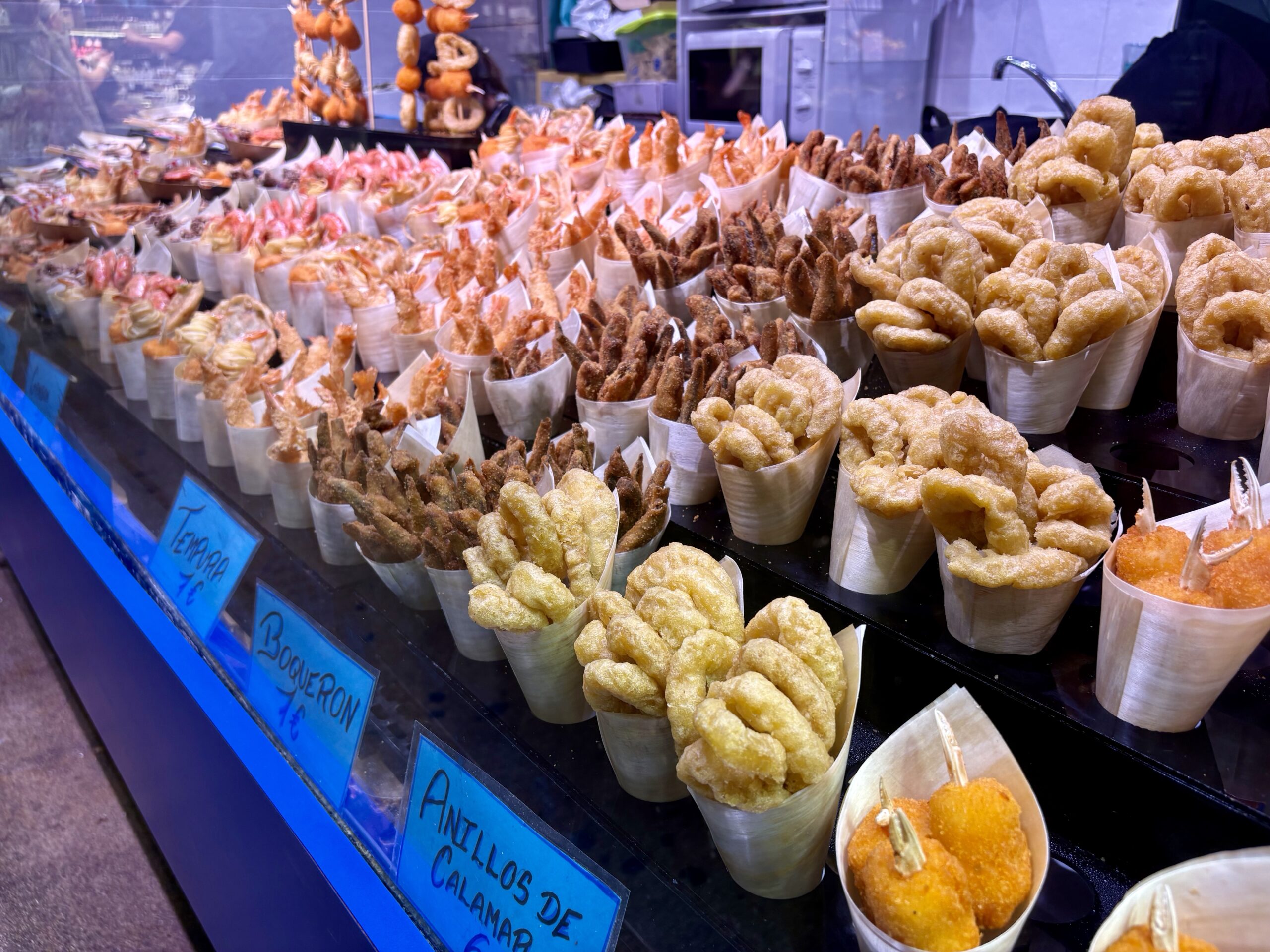 Assorted fried snacks in paper cones on a market stall display.