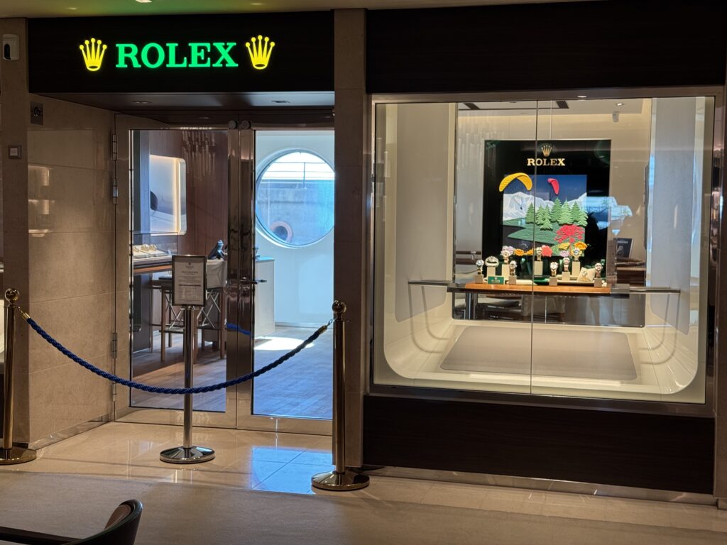 Rolex storefront in a mall with a glass display case of watches and a bright green Rolex sign above the entrance