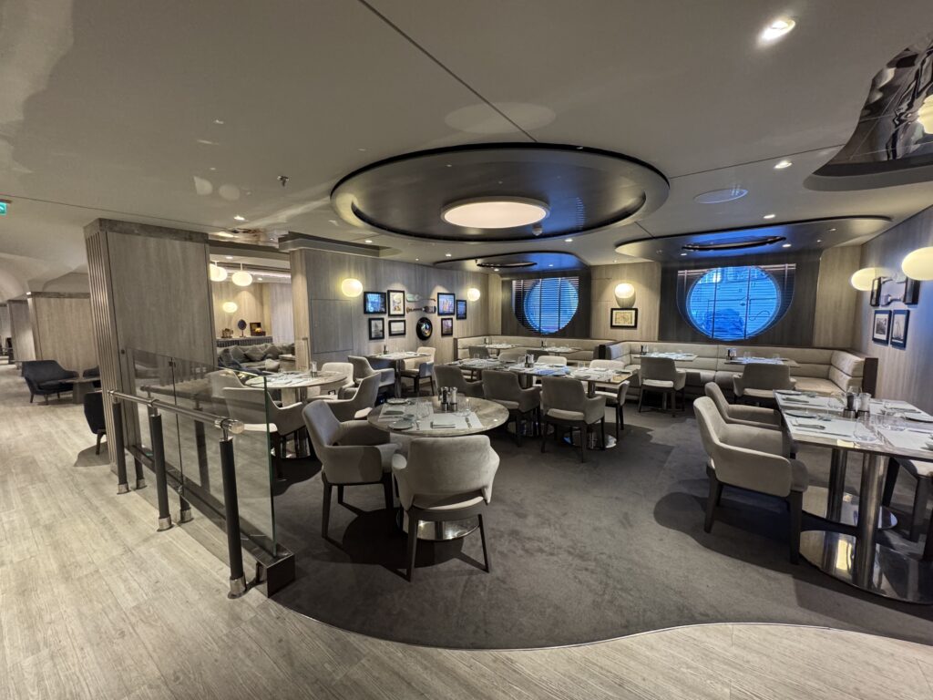 Upscale restaurant dining room with round ceiling light fixture, gray upholstered chairs, and wall gallery arranged along wood-paneled walls