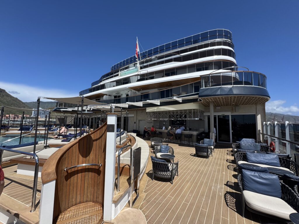 Luxurious multi-level yacht deck with wooden railings, lounge seating, and a bar beneath a clear blue sky