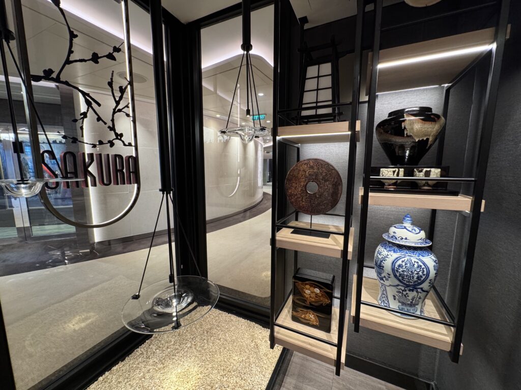 Showroom display behind glass with a black metal shelving unit, a large blue-and-white porcelain vase, and decorative ceramics.