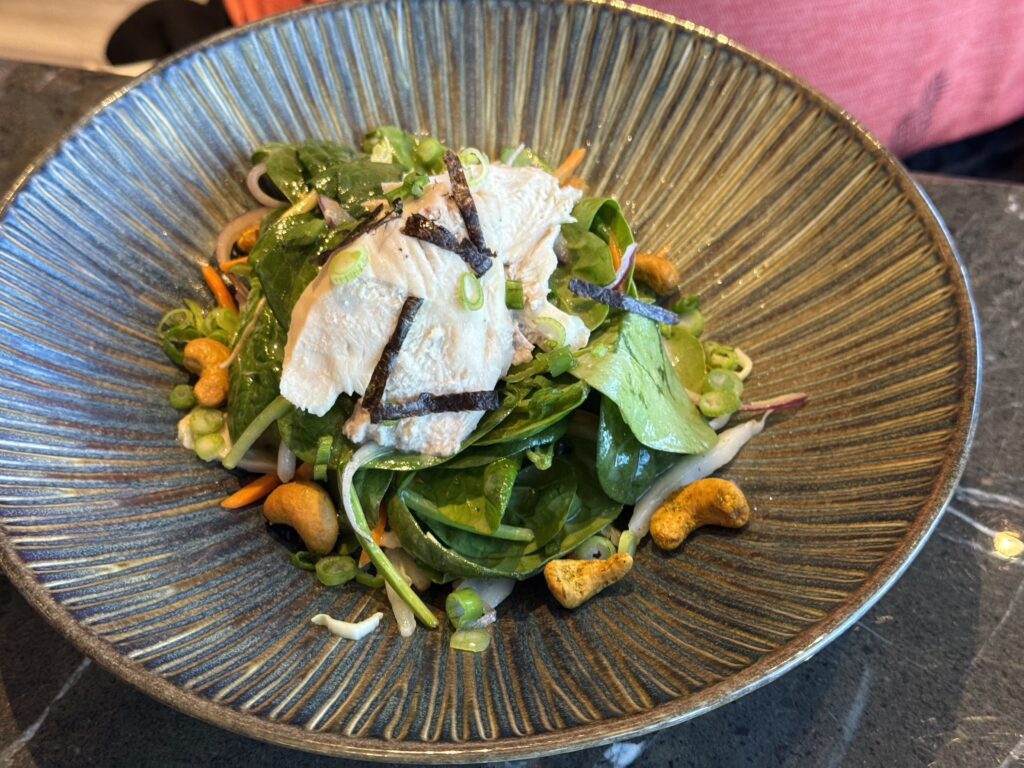 Salad bowl with sliced chicken on a bed of greens, carrot ribbons, scallions, and nori strips in a blue textured bowl.