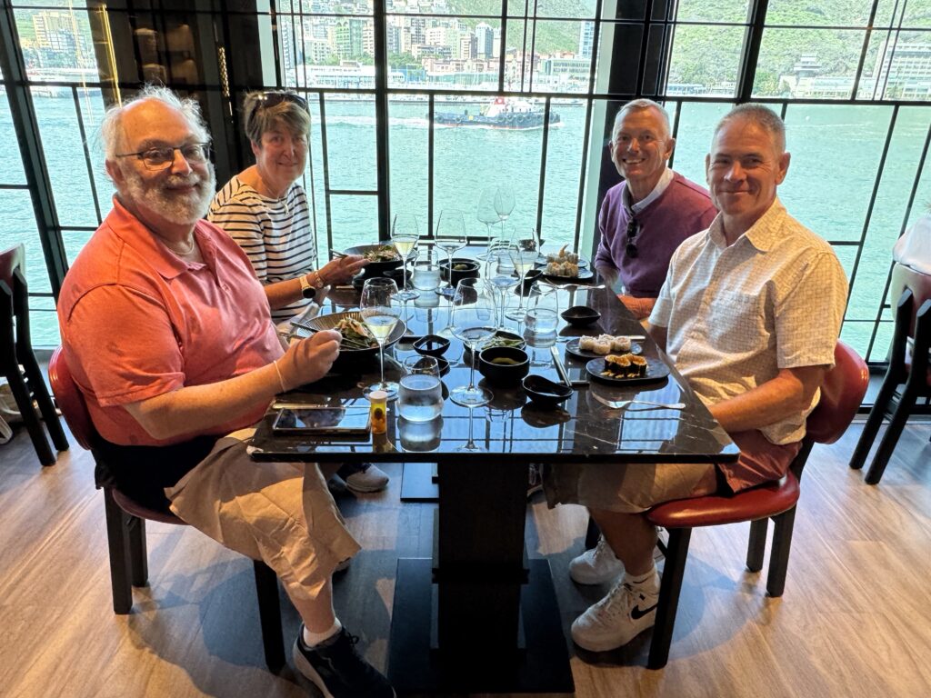 Four adults seated around a table with sushi and wine, overlooking a harbor through large glass windows.