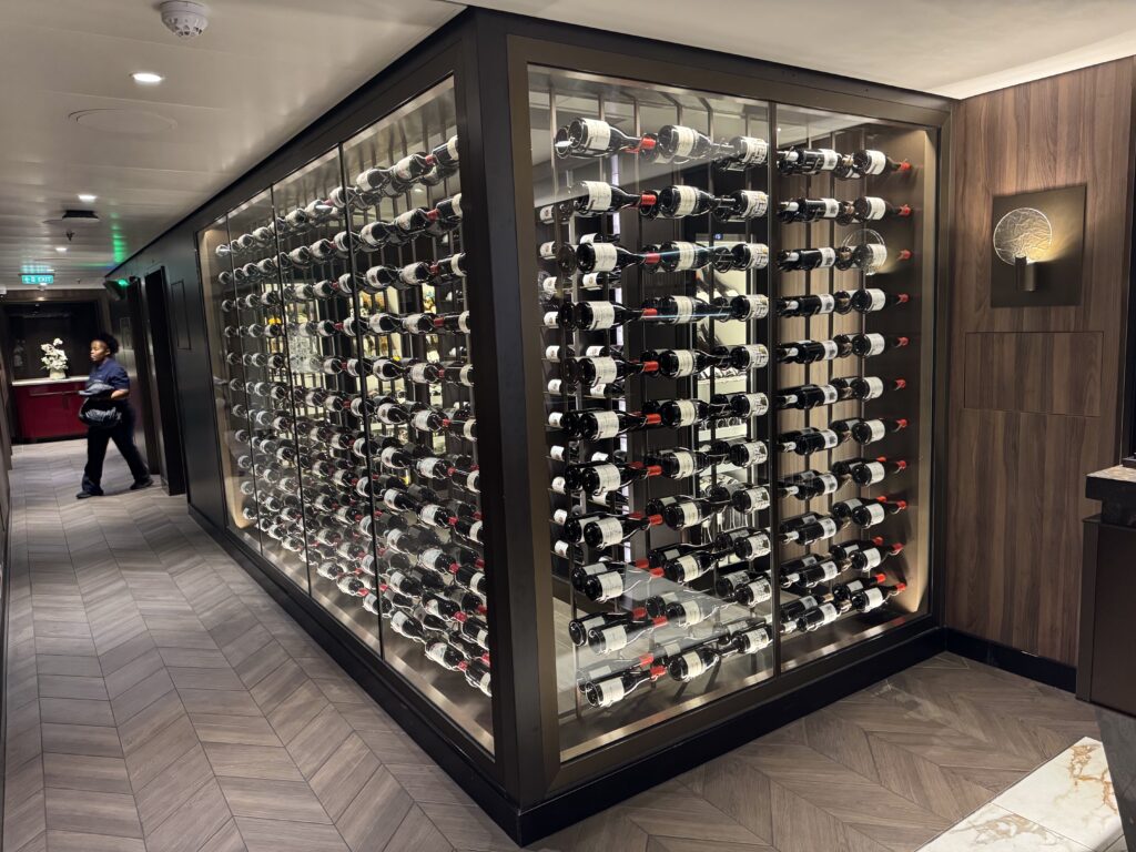 Glass-fronted wine display with many bottles organized on horizontal racks along a corridor wall in a modern interior.