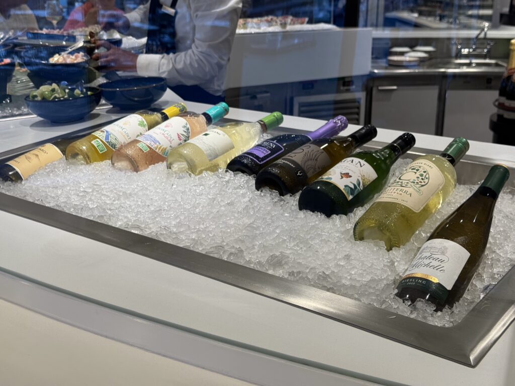 Wine bottles chill on crushed ice in a display case, with a restaurant kitchen in the background