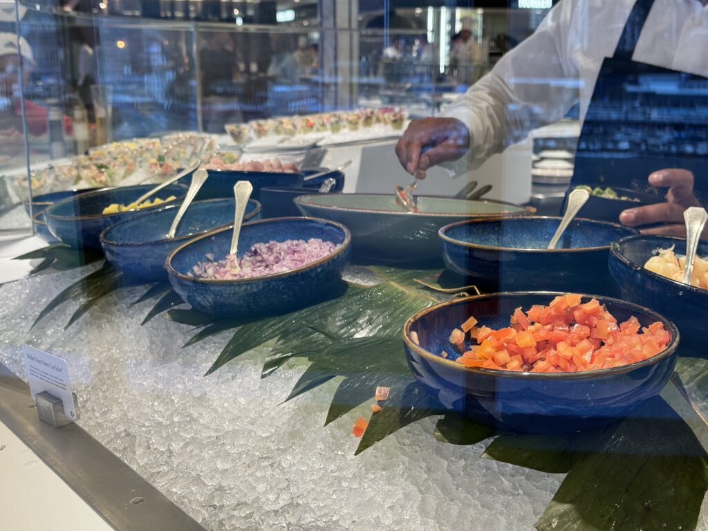 Chef in a white coat plating diced vegetables in blue bowls behind a glass sushi counter.