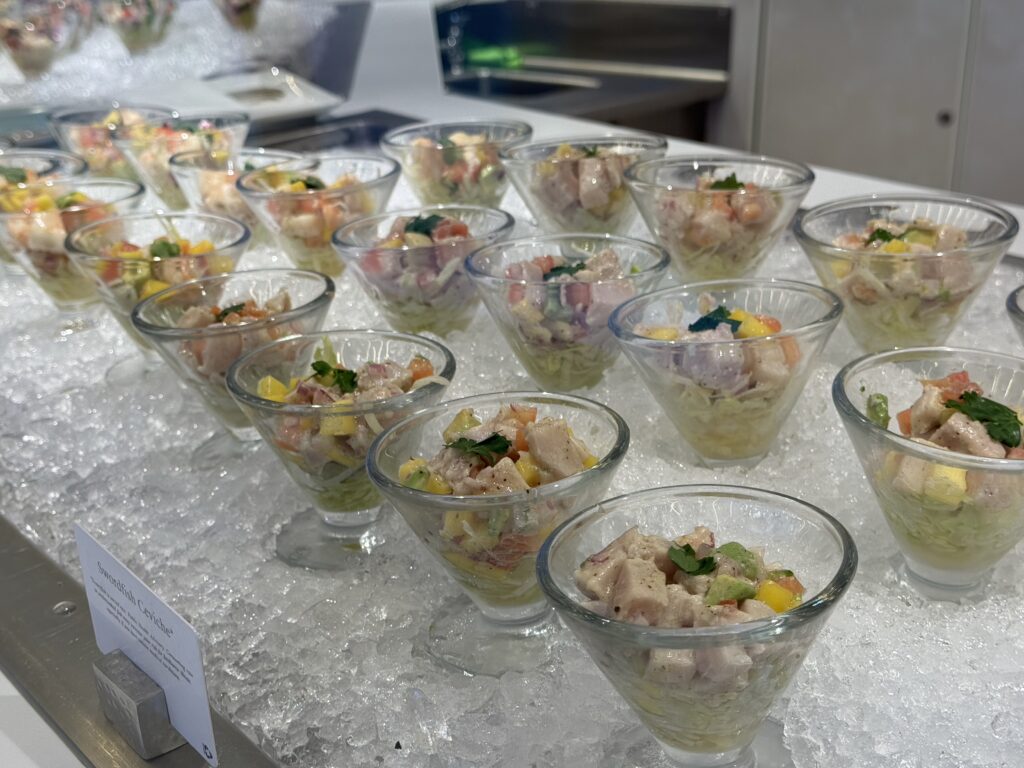 Glass cups of colorful fish ceviche with diced mango, peppers, and herbs on crushed ice, ready to serve.