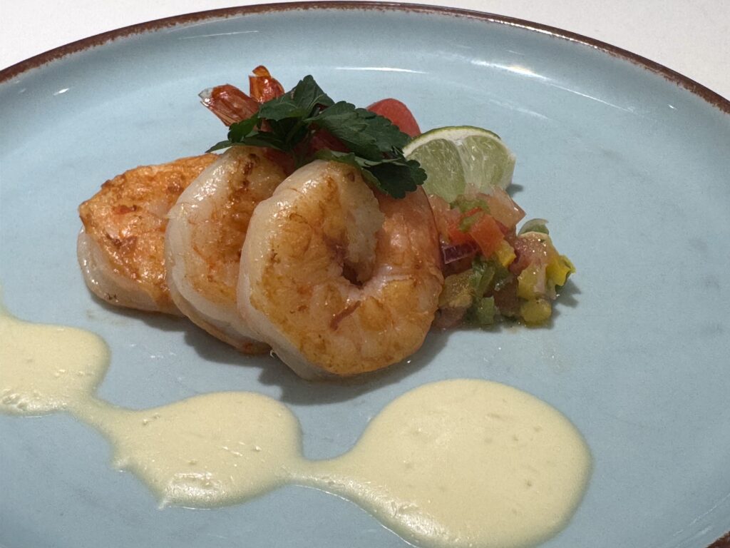 Shrimp arranged on a light blue plate with lime, fresh herbs, and pale sauce dollops around the edge.