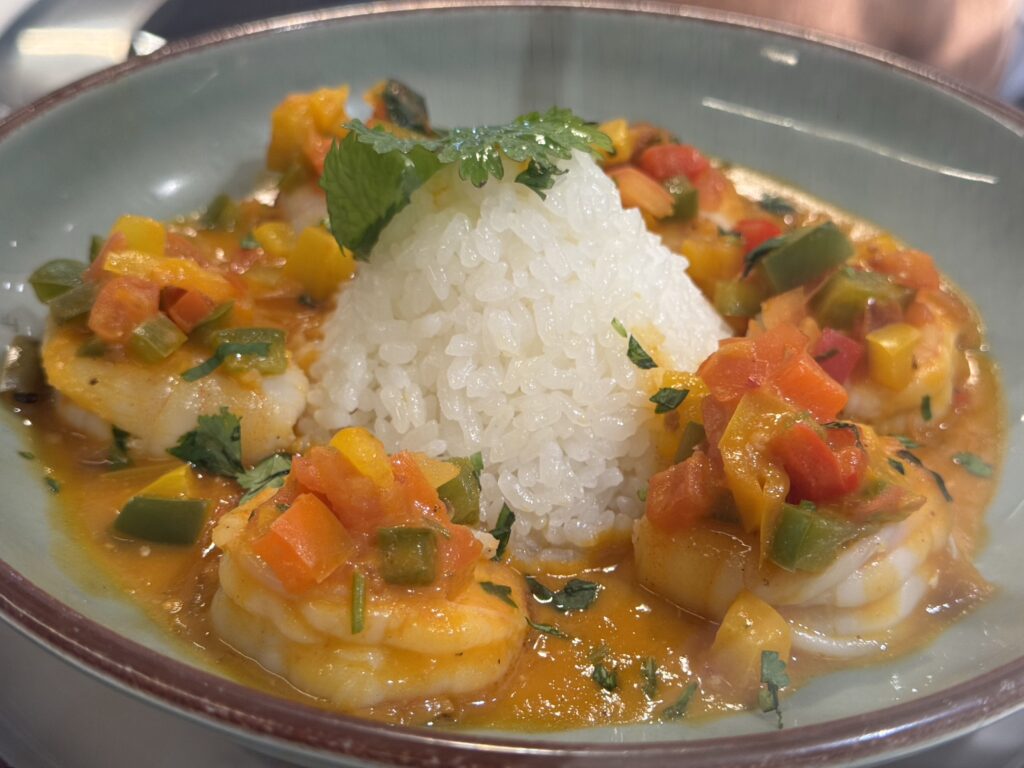 Mounded white rice topped with parsley, surrounded by shrimp and colorful vegetable curry in an orange sauce.