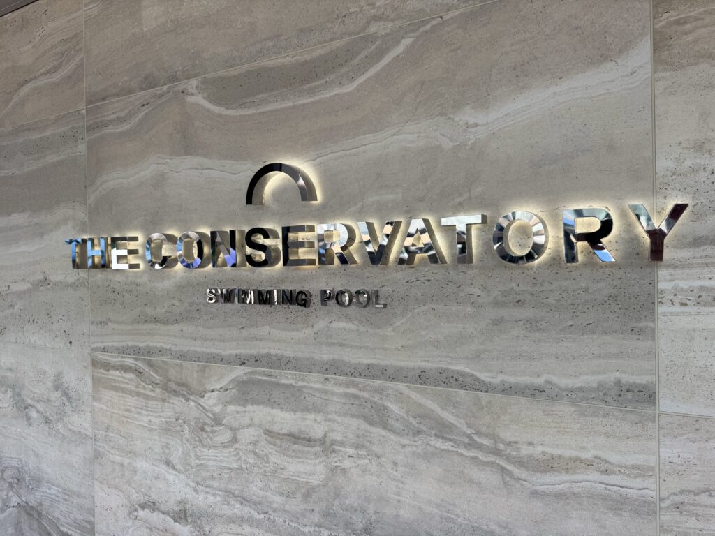 Metallic sign on a beige marble wall reading 'THE CONSERVATORY' with 'SWIMMING POOL' below.