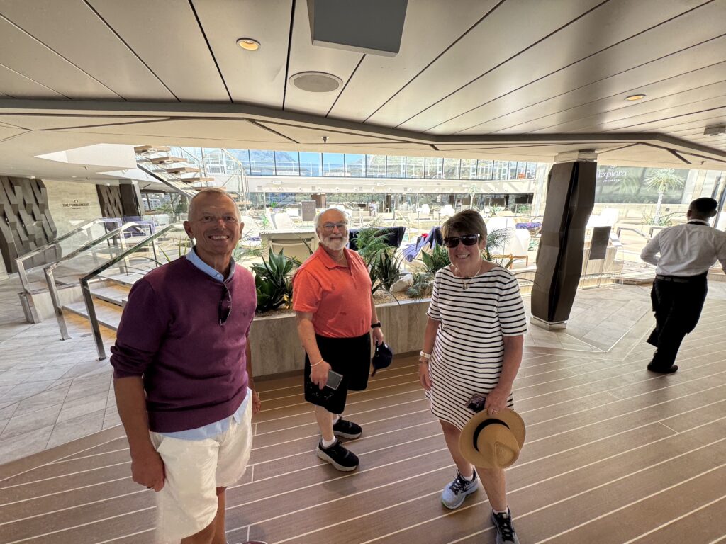 Three smiling adults stand inside a modern atrium with stairs and glass walls in the background, posing for a photo.