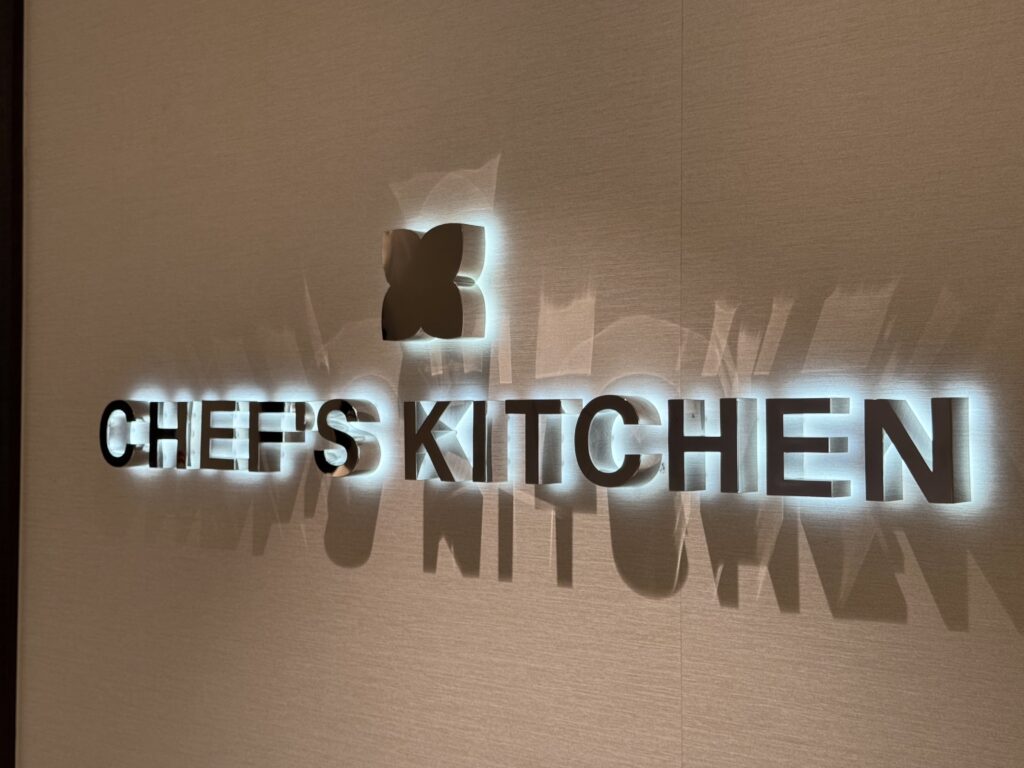 Backlit wall sign reading CHEESE KITCHEN with a butterfly silhouette casting light and shadow on the beige wall.