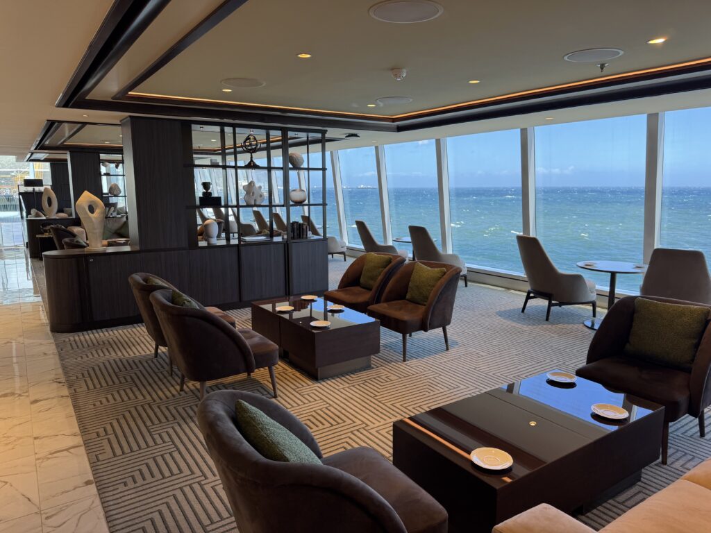 Luxurious lounge with brown leather chairs, glass tables, and large windows overlooking the ocean.