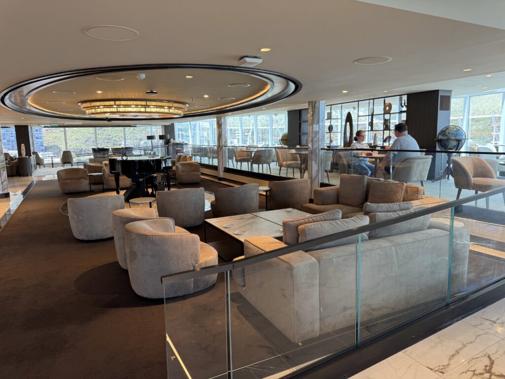 Luxurious hotel lounge with beige seating, marble tables, and a circular illuminated ceiling fixture near a glass railing.