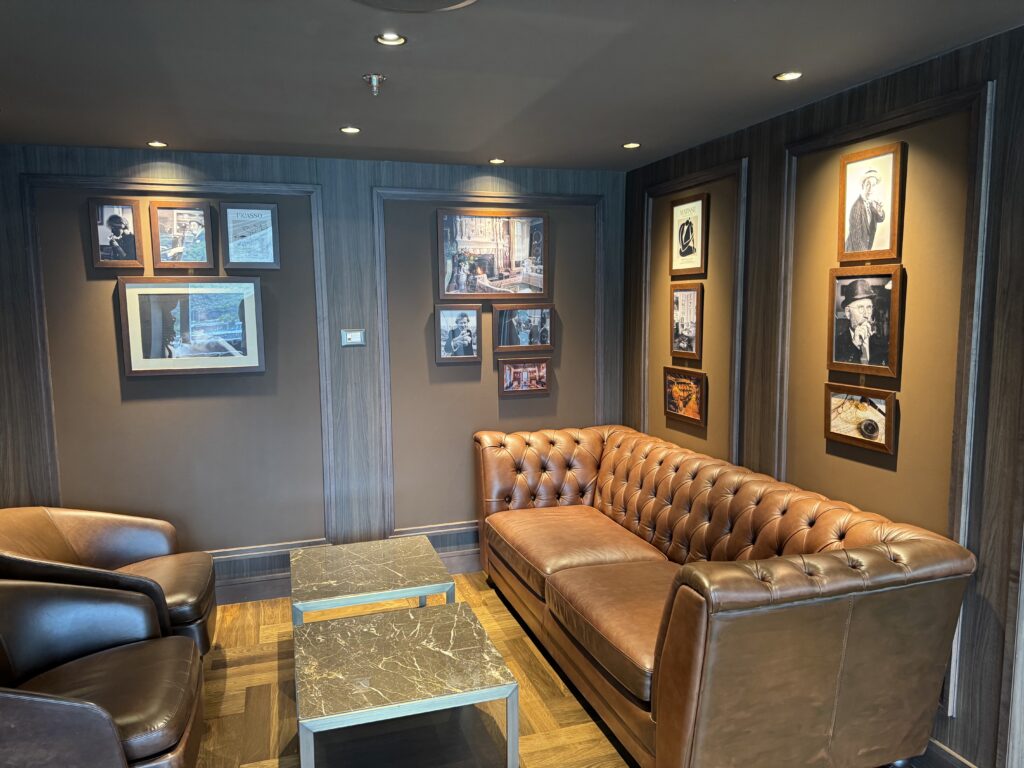 Cozy lounge with brown tufted leather sofas, gray marble-topped tables, and framed art on dark wood walls.
