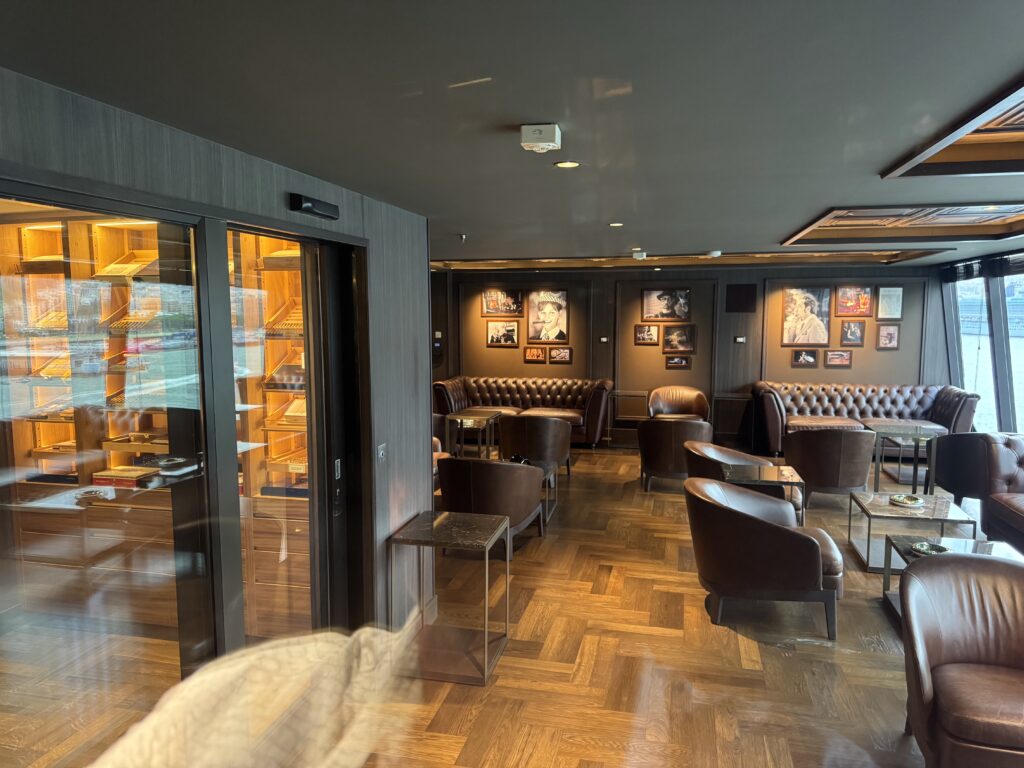 Lounge area with dark walls, brown leather Chesterfield sofas, glass coffee tables, and framed photos on the wall.