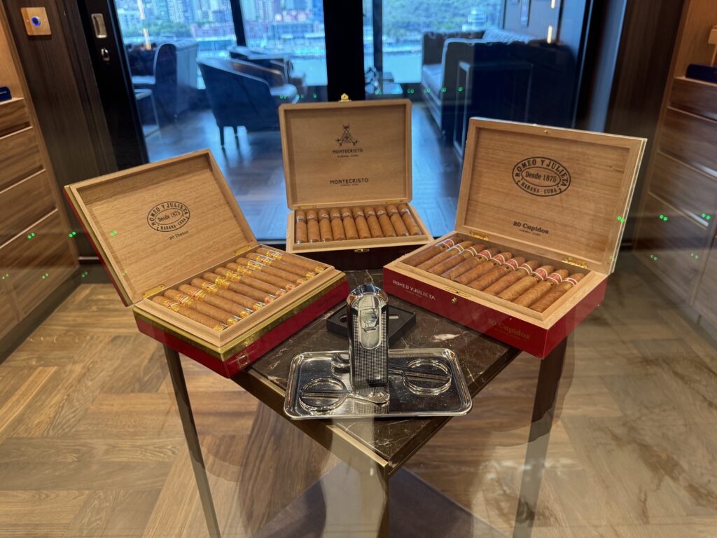 Open wooden cigar boxes with Montecristo labels and cigars arranged on a glass table in a showroom.