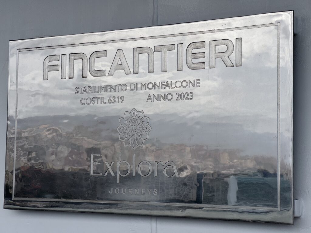 Metal plaque with embossed 'FINCANTIERI' logo and Italian text reading 'Stabilimento di Monfalcone, Costr. 6319, Anno 2023' plus a decorative emblem beneath.