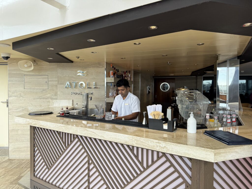 Bar counter with a bartender preparing drinks; bottles and glassware behind him in a modern, marble-toned lounge.