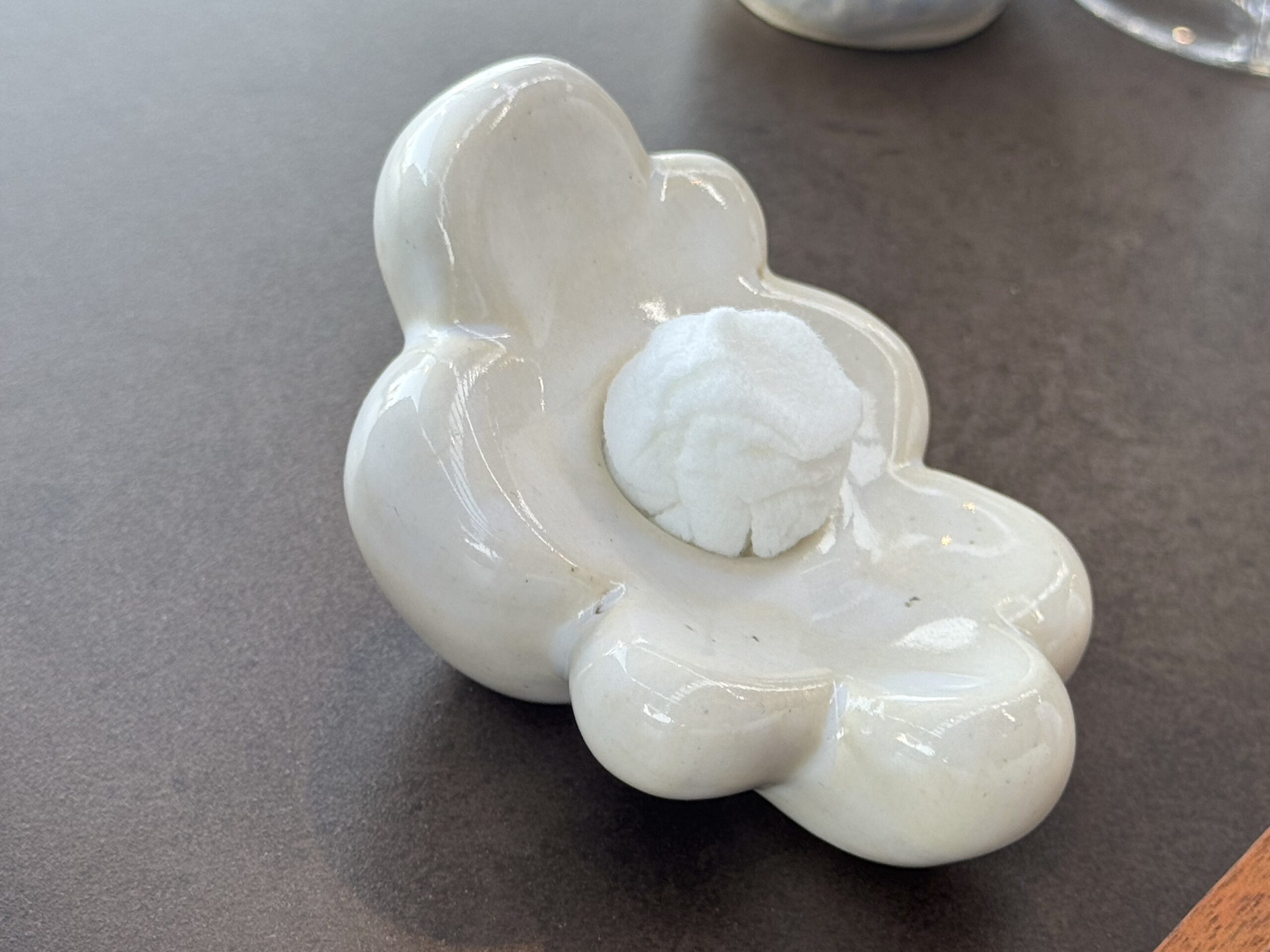 Close-up of a glossy pale blue ceramic sculpture with rounded lobes on a dark surface.
