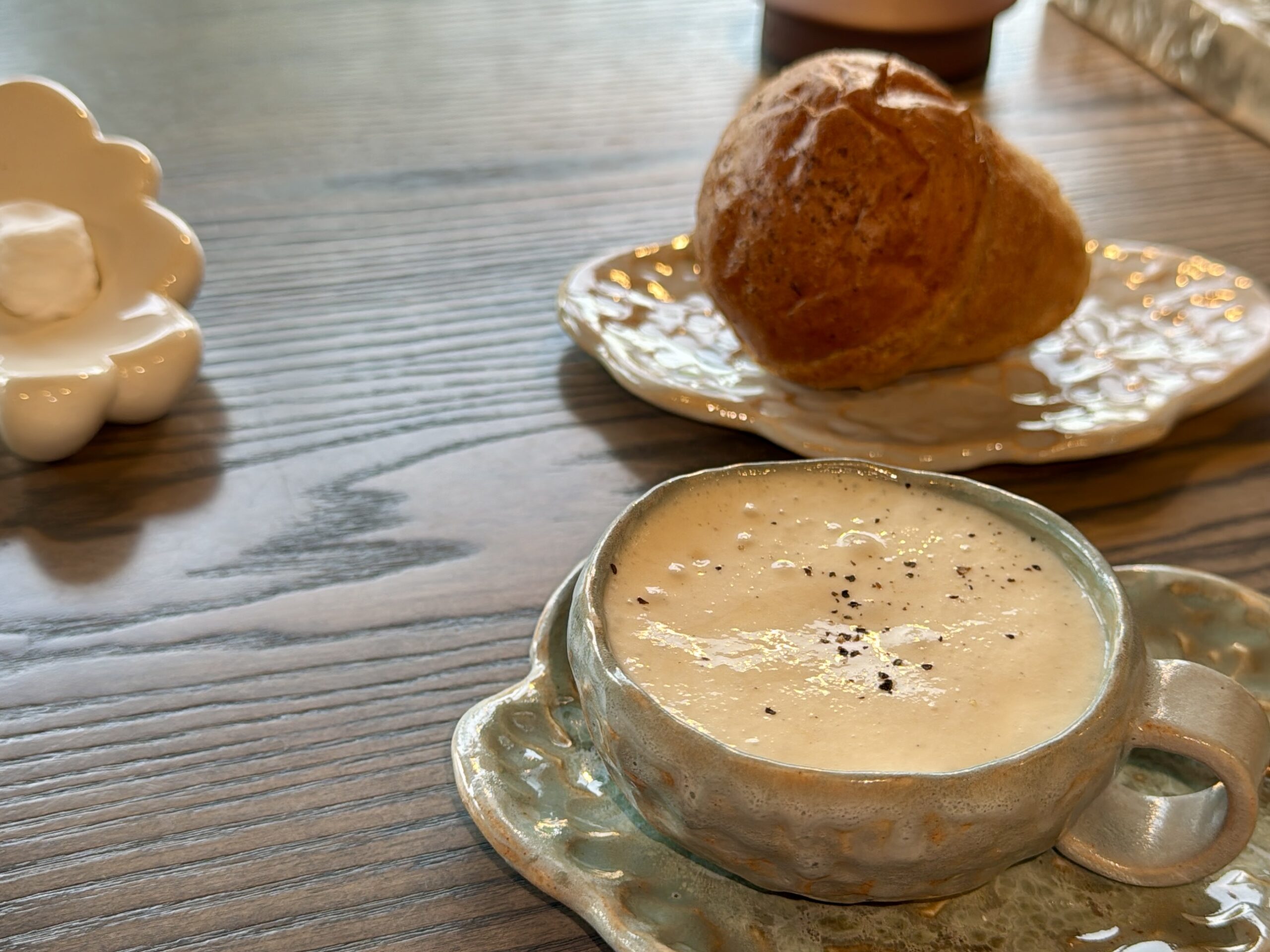 Creamy soup in a rustic ceramic cup on a wooden table, with a pastry on a plate nearby.