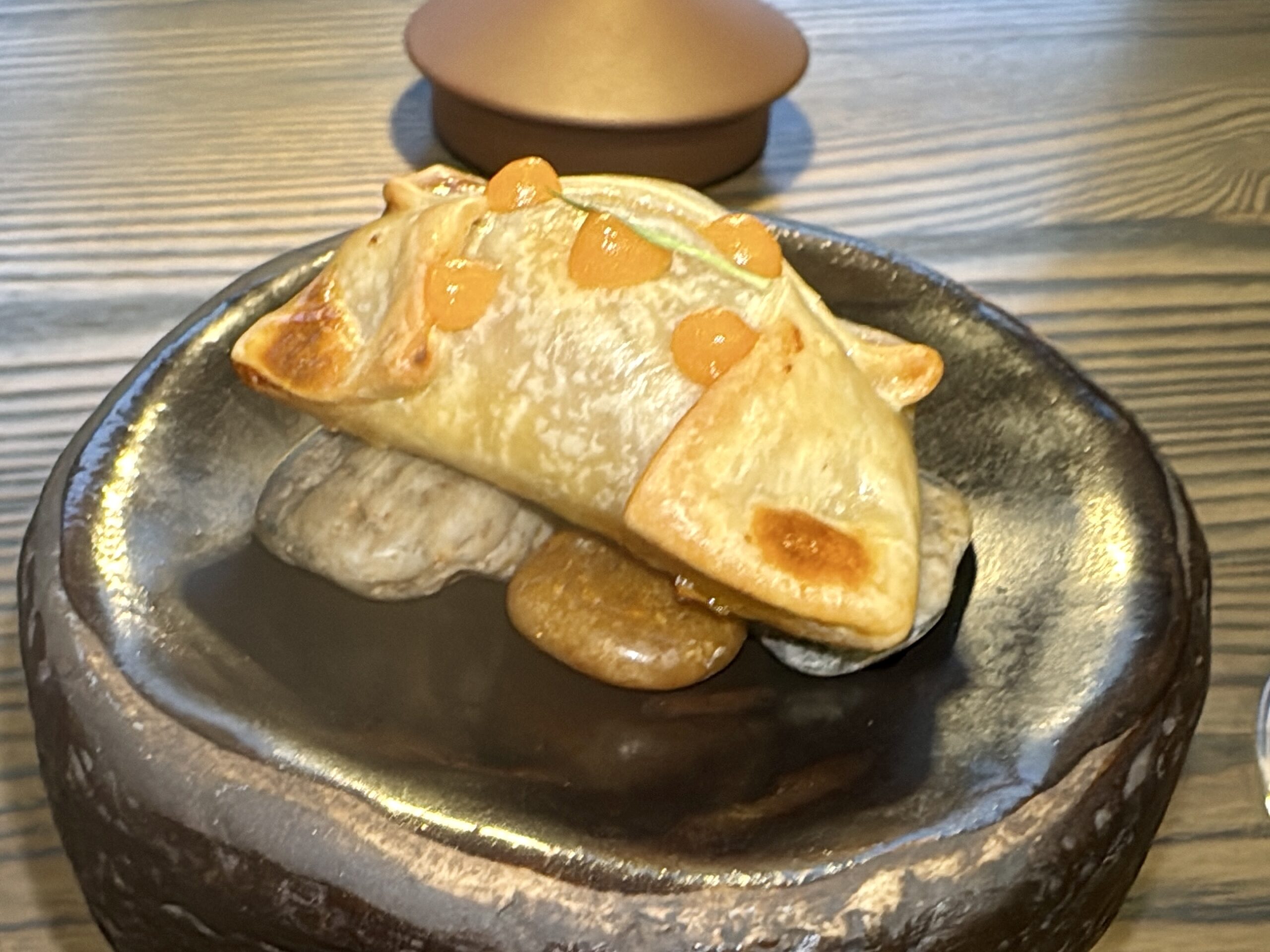 Flaky pastry topped with small orange candy pieces on a dark plate, close-up view on a wooden table.