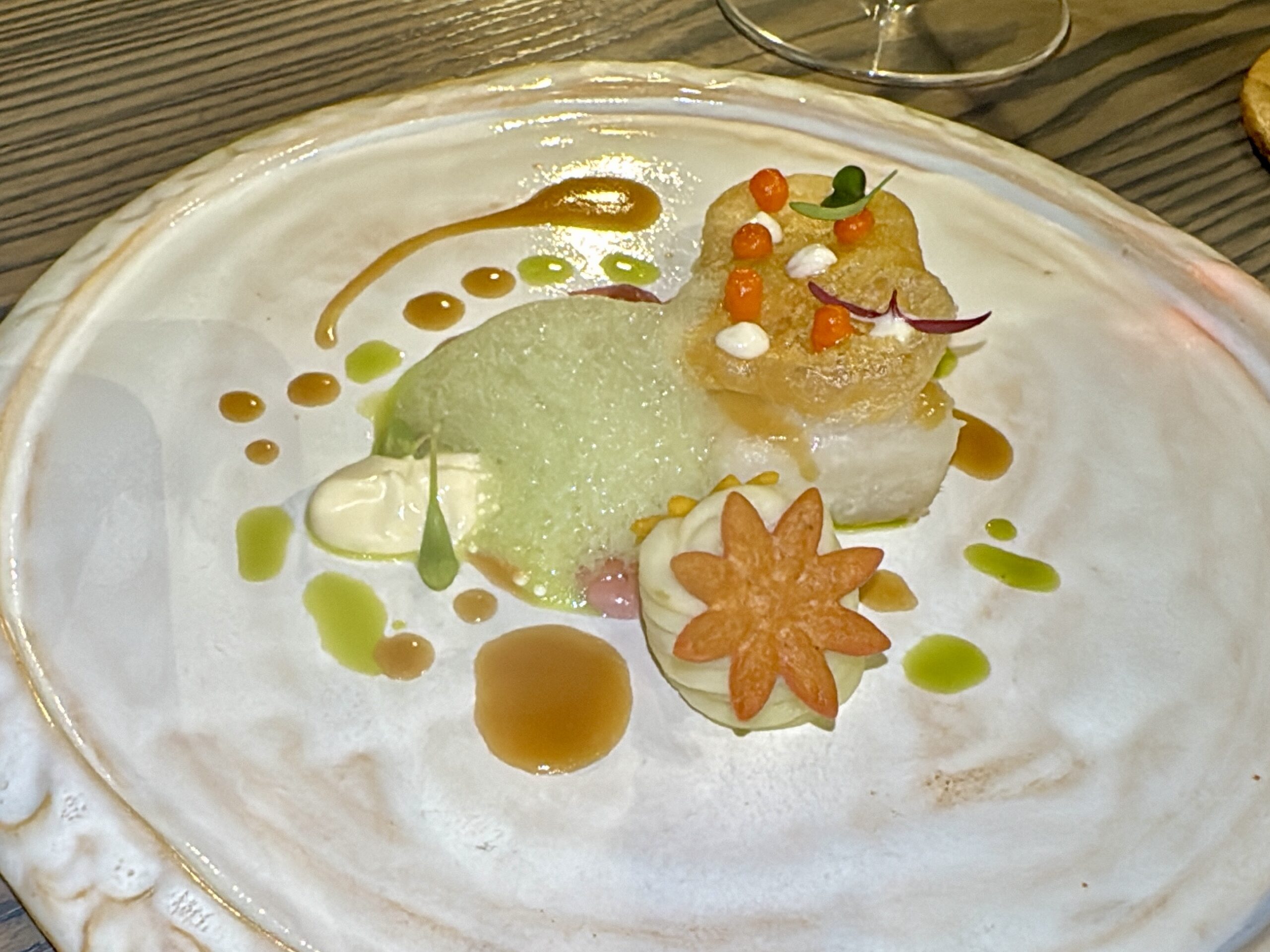 Plate with a quenelle of pale green sorbet, carrot flower garnish, and dotted sauces as artistic plating.