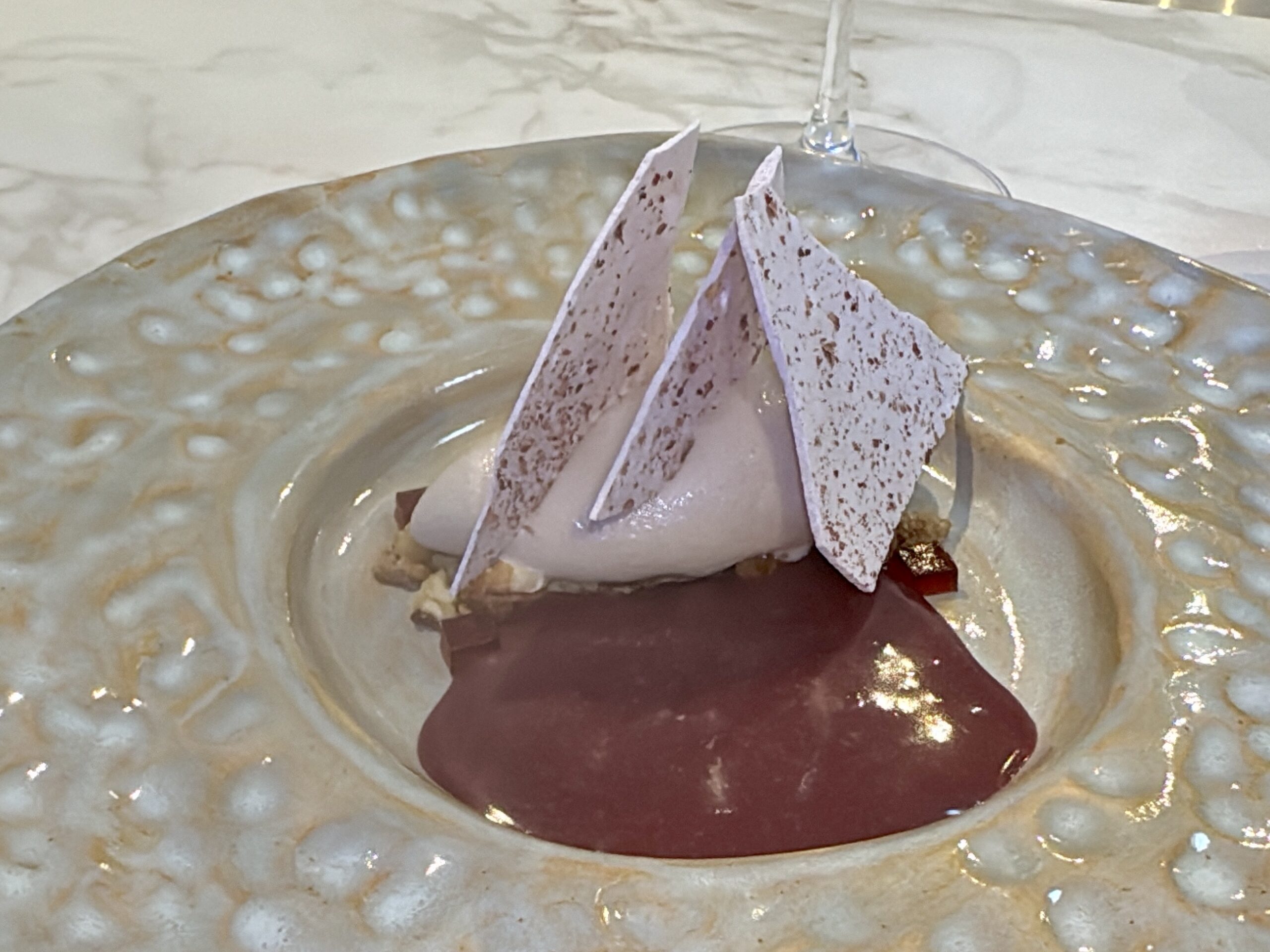 Dessert plate with pink chocolate shards standing upright over a pool of dark chocolate sauce on a speckled, pale ceramic dish.