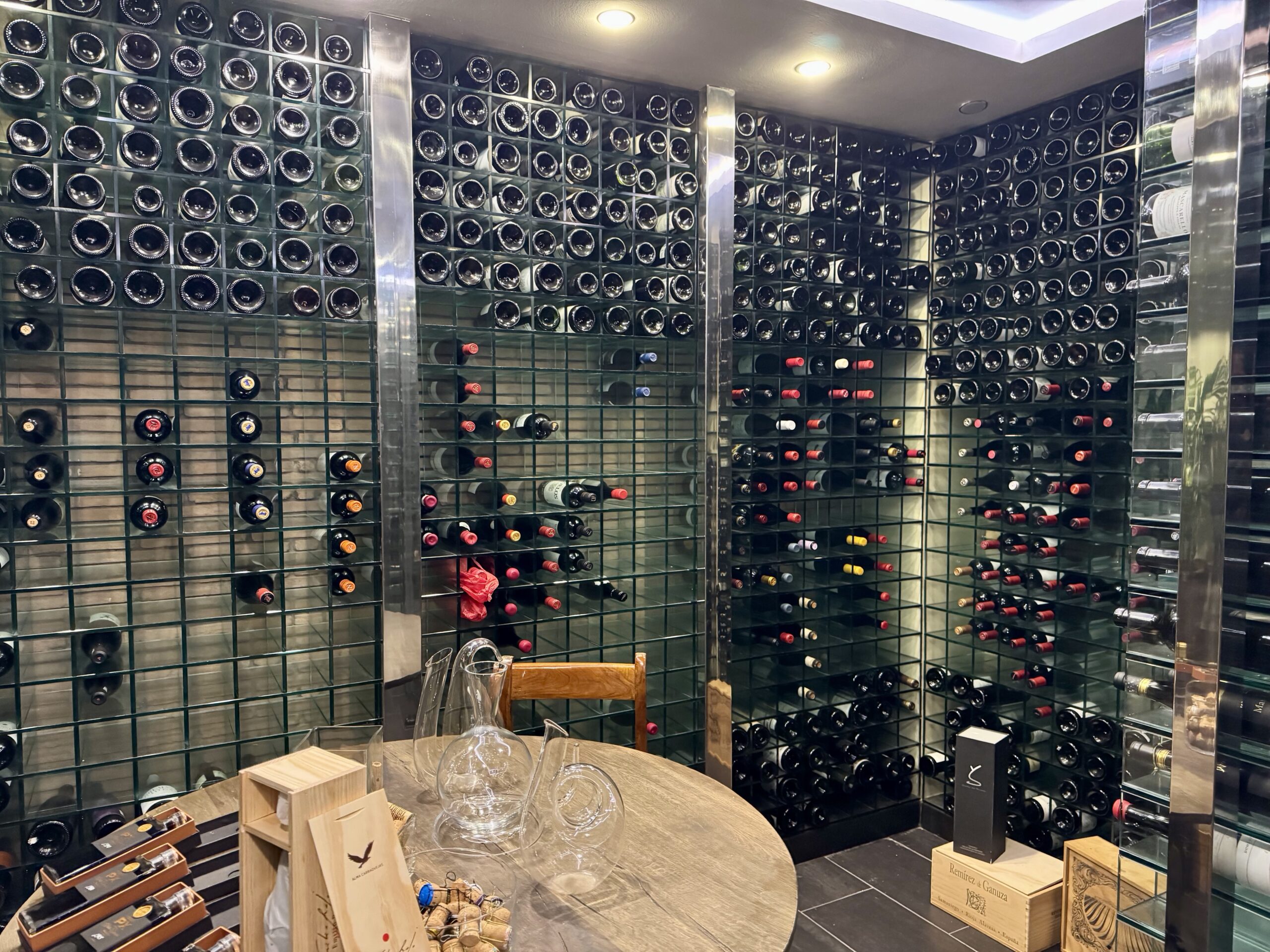 Wine cellar with floor-to-ceiling racks of bottles and a round table with glassware in the foreground.