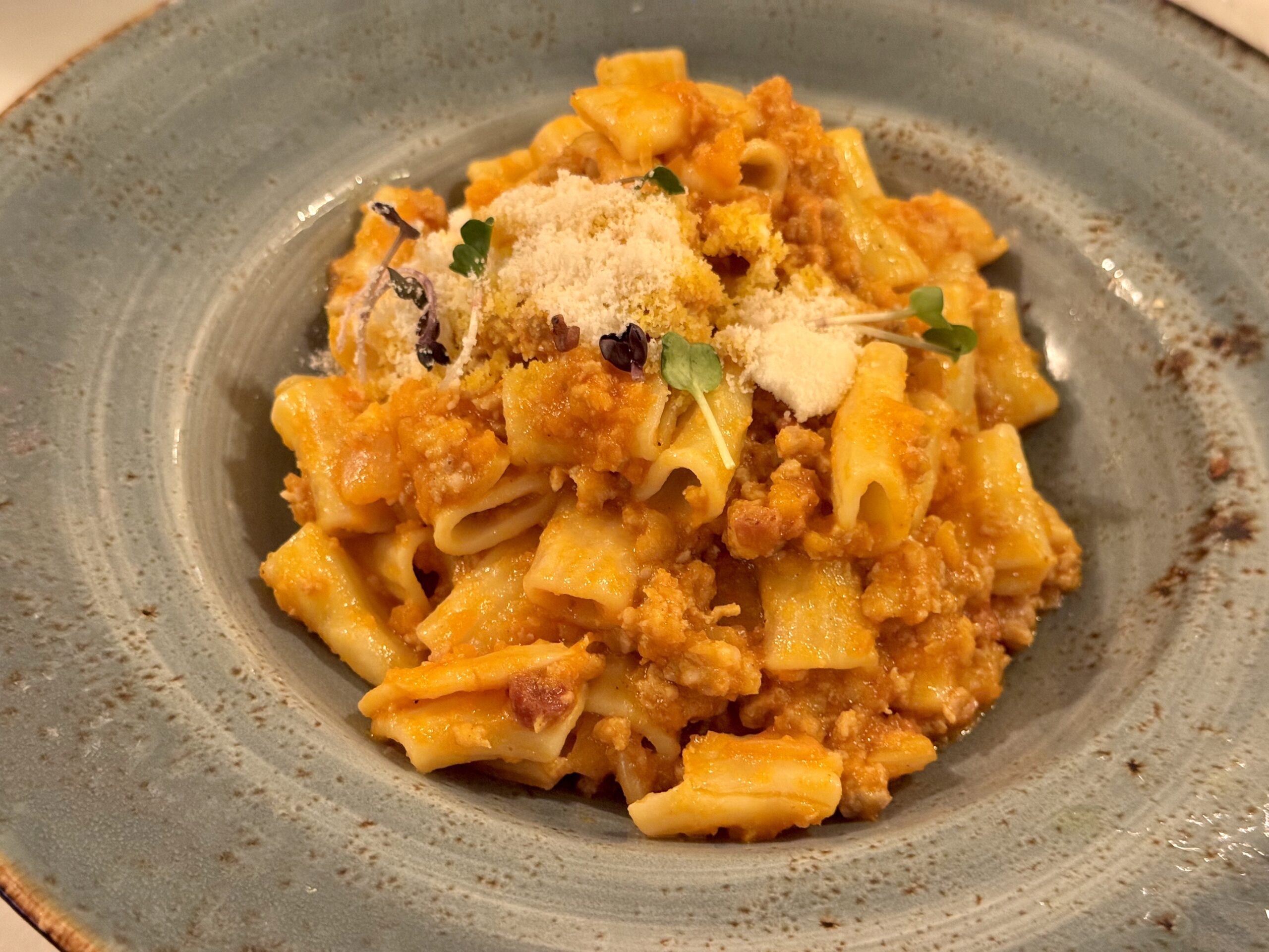 Penne pasta in an orange creamy sauce topped with grated cheese and microgreens on a gray ceramic plate (close-up).