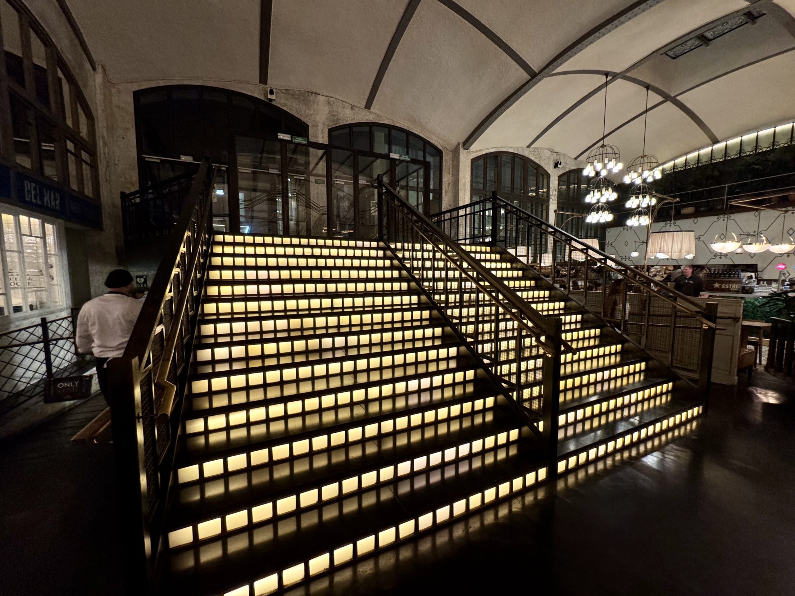 Interior of a historic building with glowing step-lit staircase and black metal railings leading to a second level.
