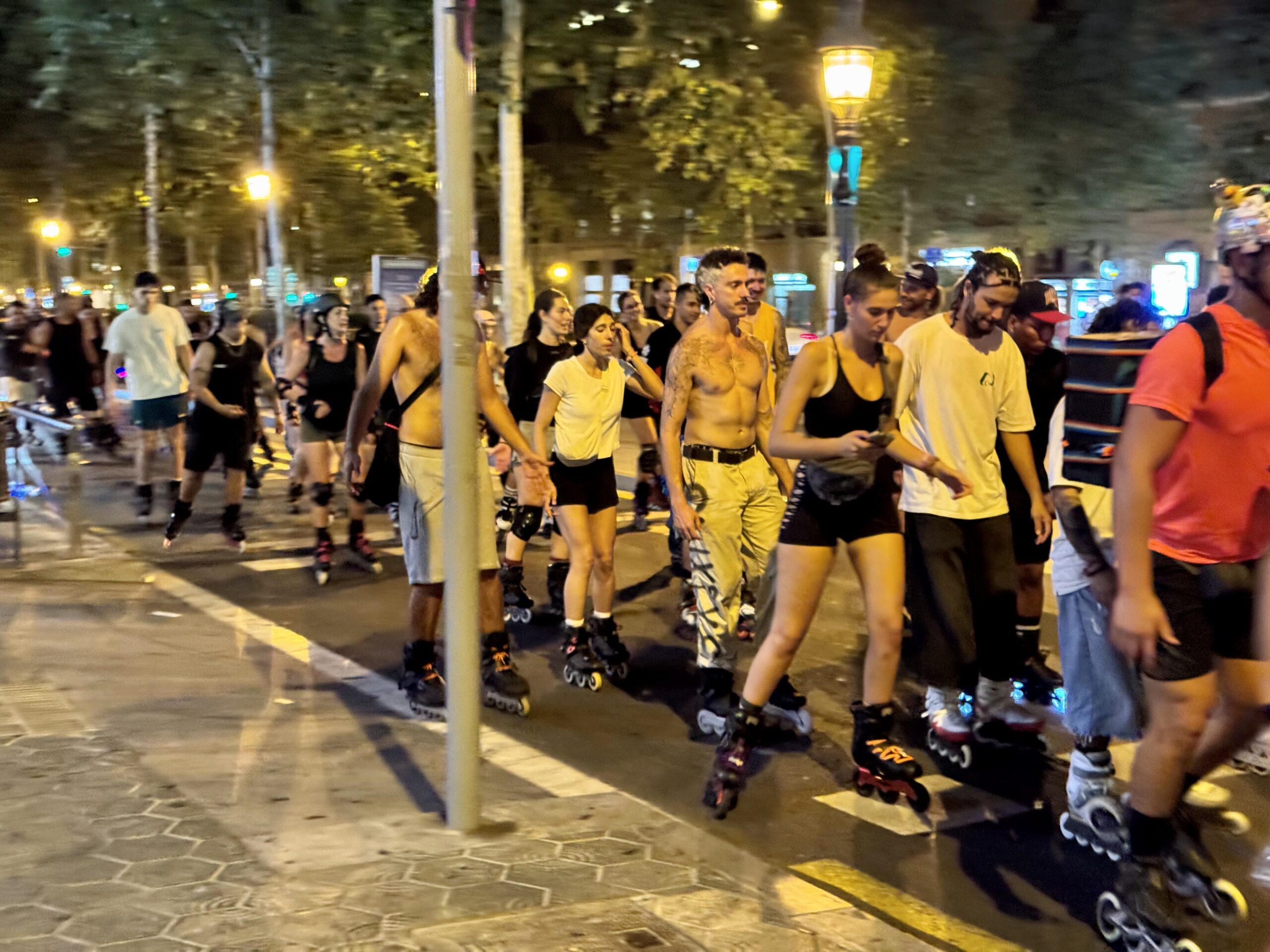 Large group of people inline skating down a city street at night with streetlights.