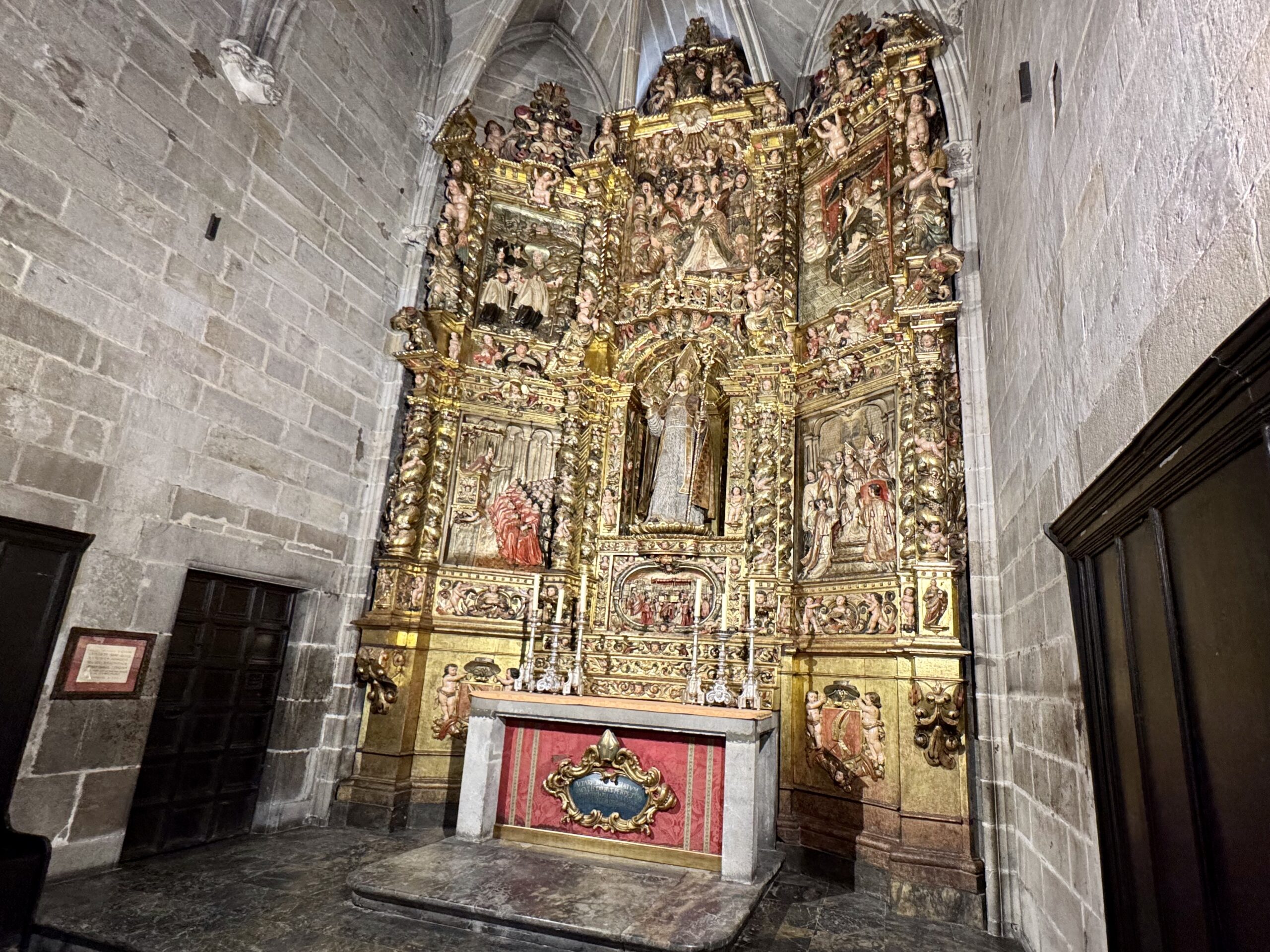 Ornate gold-toned church altarpiece with numerous carved figures and religious scenes against stone walls.