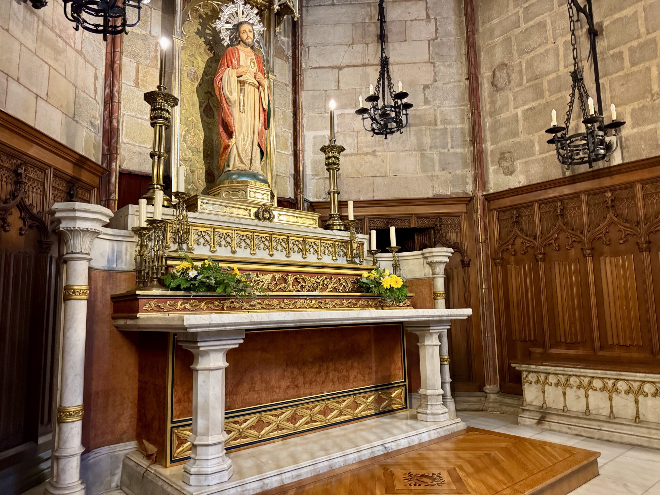 Altar in a church with a gilded statue of a saint, ornate gold details, and lit candles on both sides.