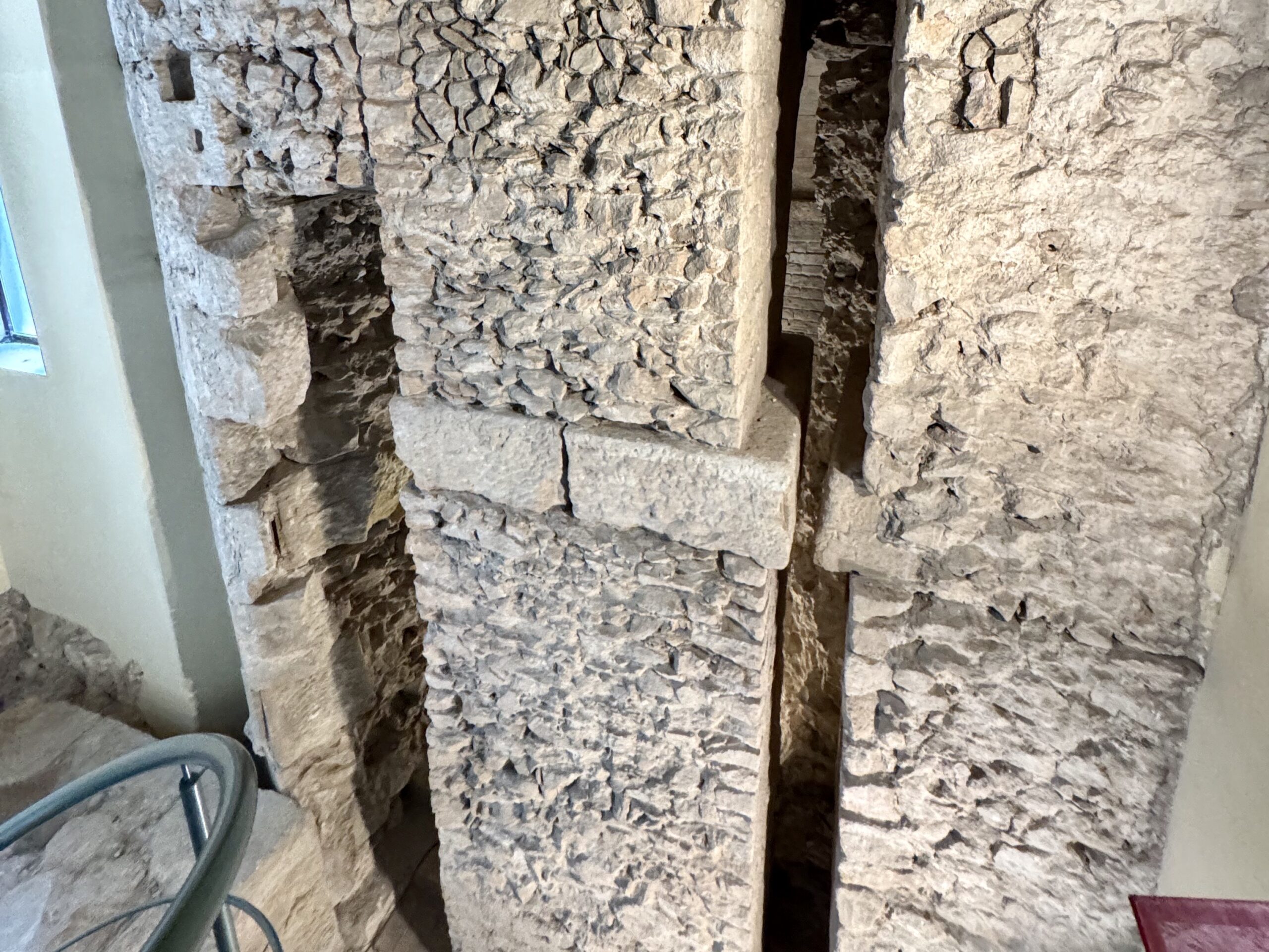 Exposed rough stone wall with a narrow vertical gap between blocks; a coiled blue-green hose rests in the foreground on the left.