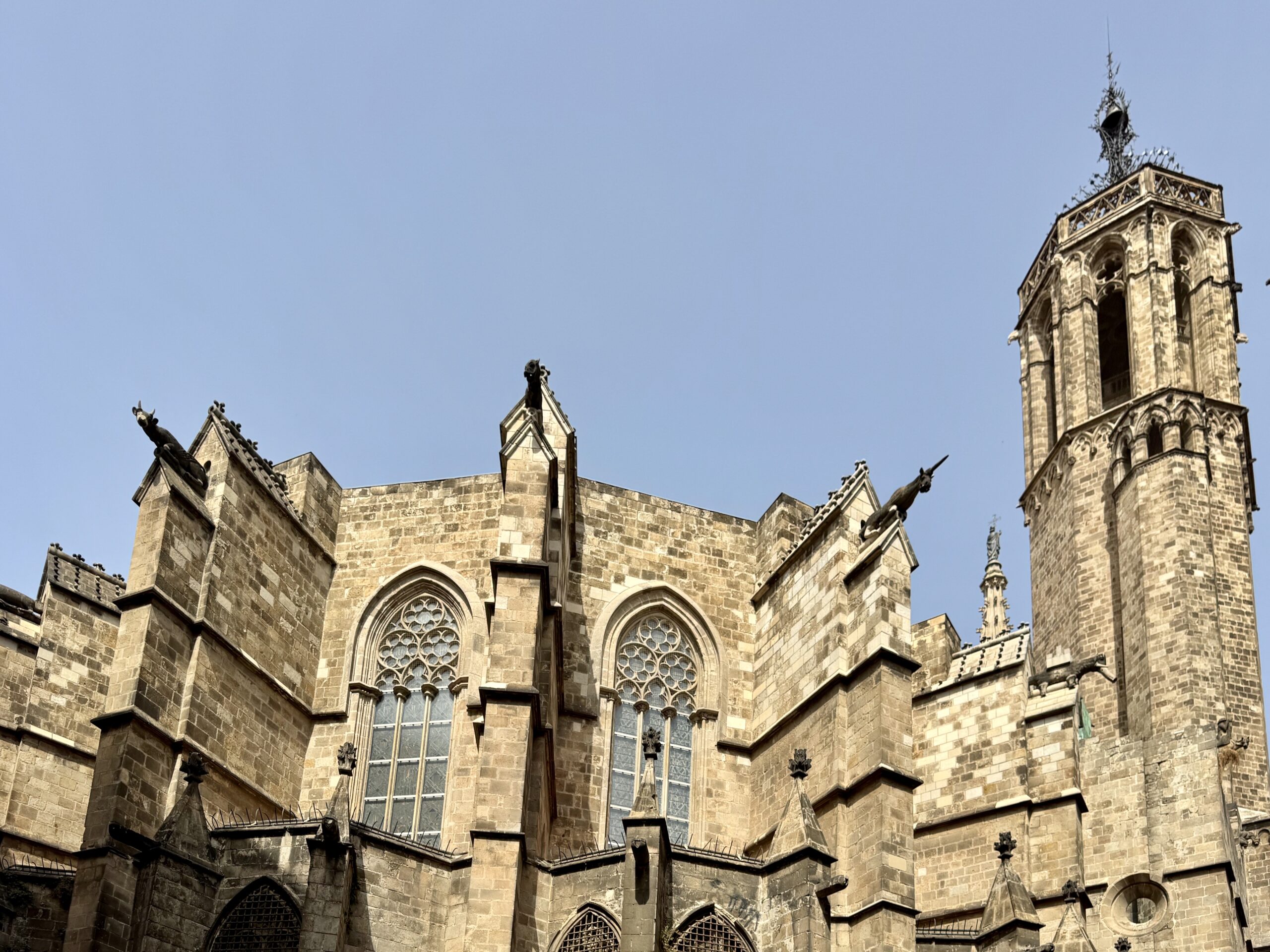 Gothic cathedral facade with arched windows and decorative gargoyles against a clear blue sky.