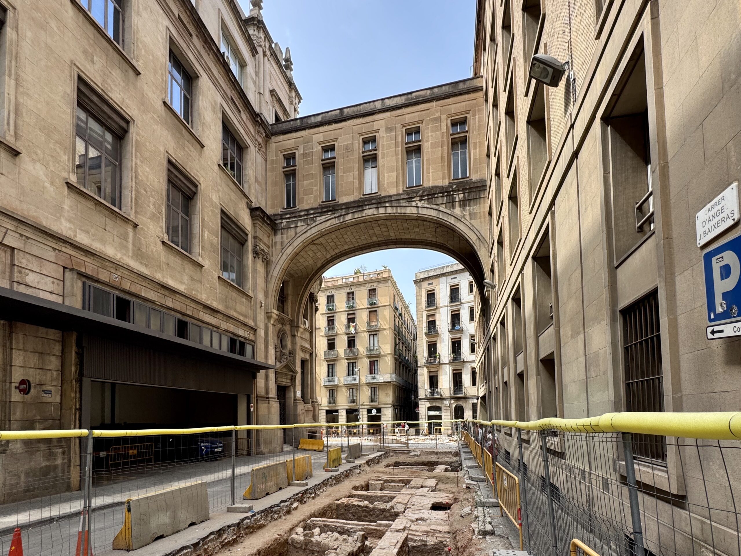 Narrow city street under a stone archway with construction barriers and rubble along the road behind fencing.