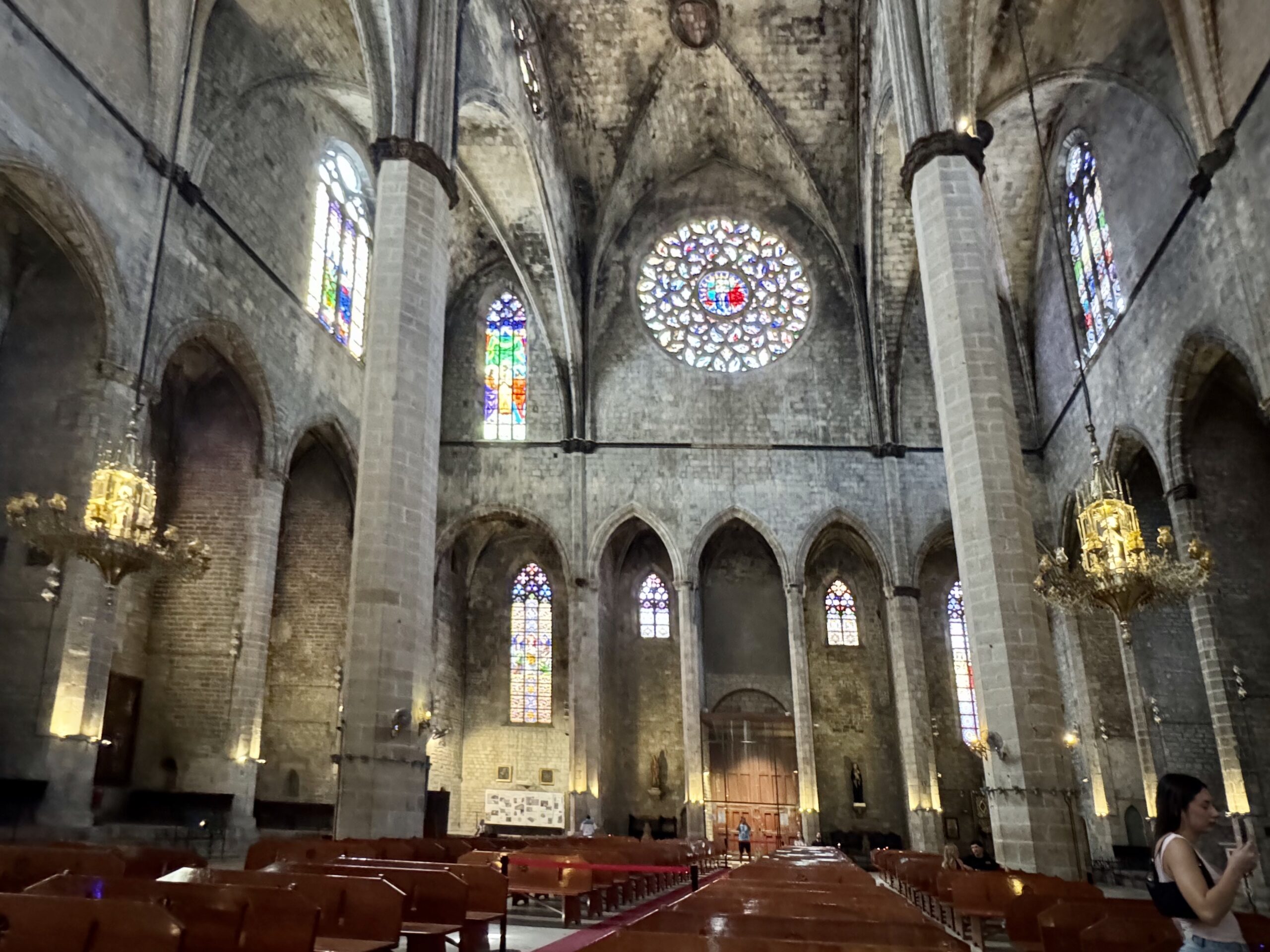 Inside Gothic cathedral: tall stone columns, vaulted ceilings, and colorful stained-glass windows with wooden pews in the foreground