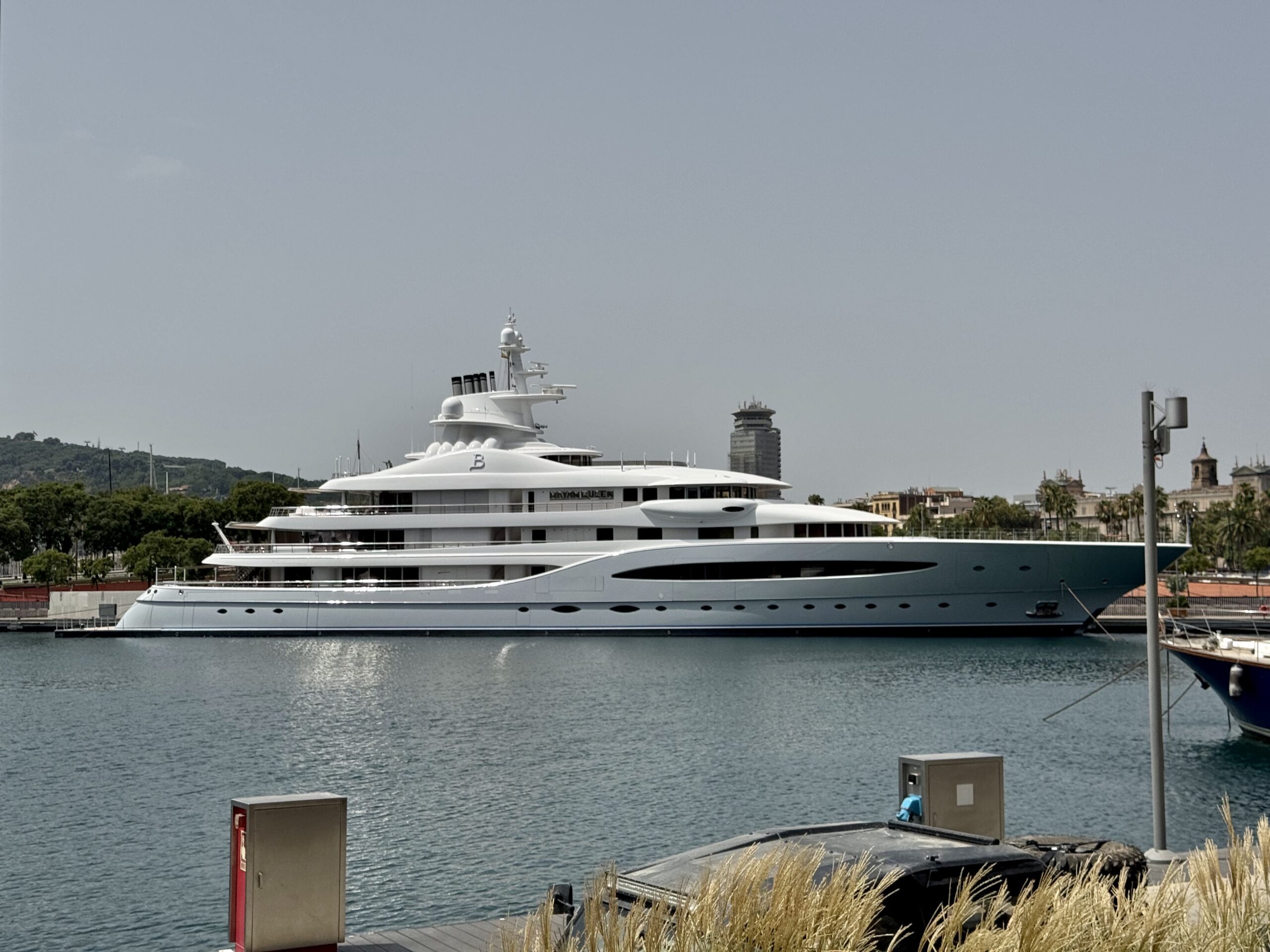 White luxury yacht moored at a marina with calm water and distant city buildings on the horizon