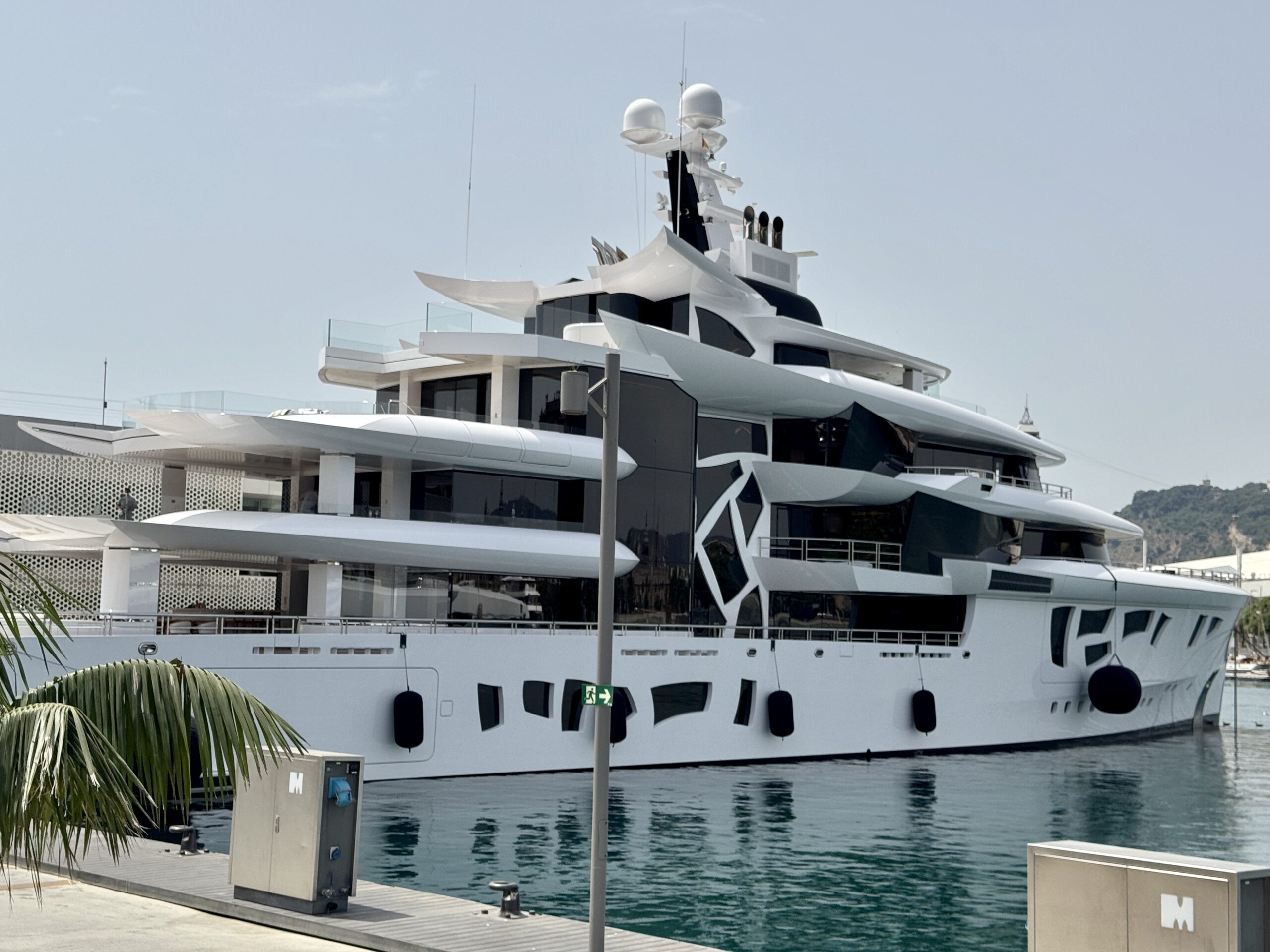 White luxury motor yacht moored at a marina with glass railings and calm water nearby.