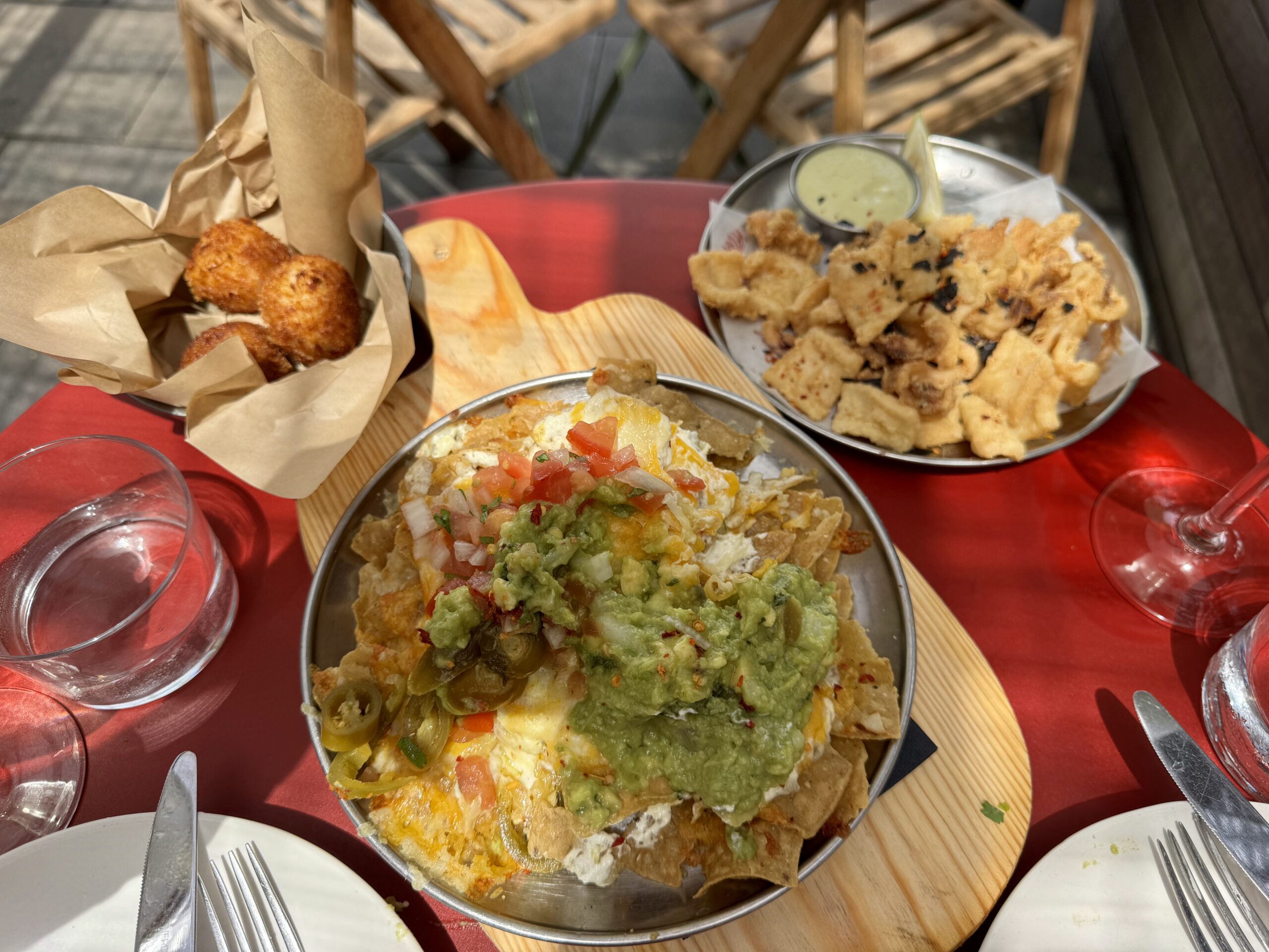 Plate of loaded nachos topped with guacamole, pico de gallo, and melted cheese on a red table with a side of green dipping sauce.
