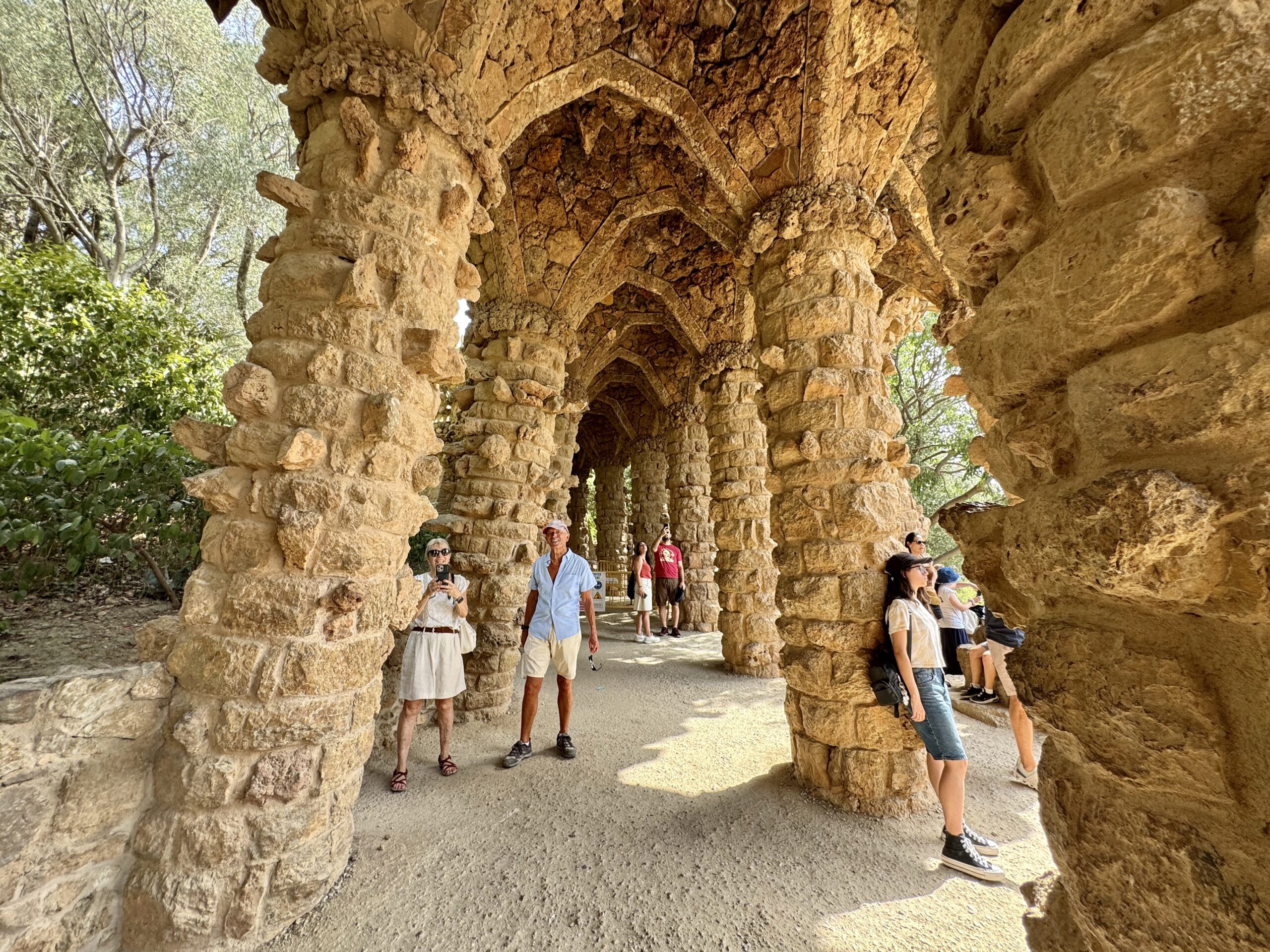 Stone archway corridor formed from rugged rock columns; several tourists stand and pose beneath the arches.