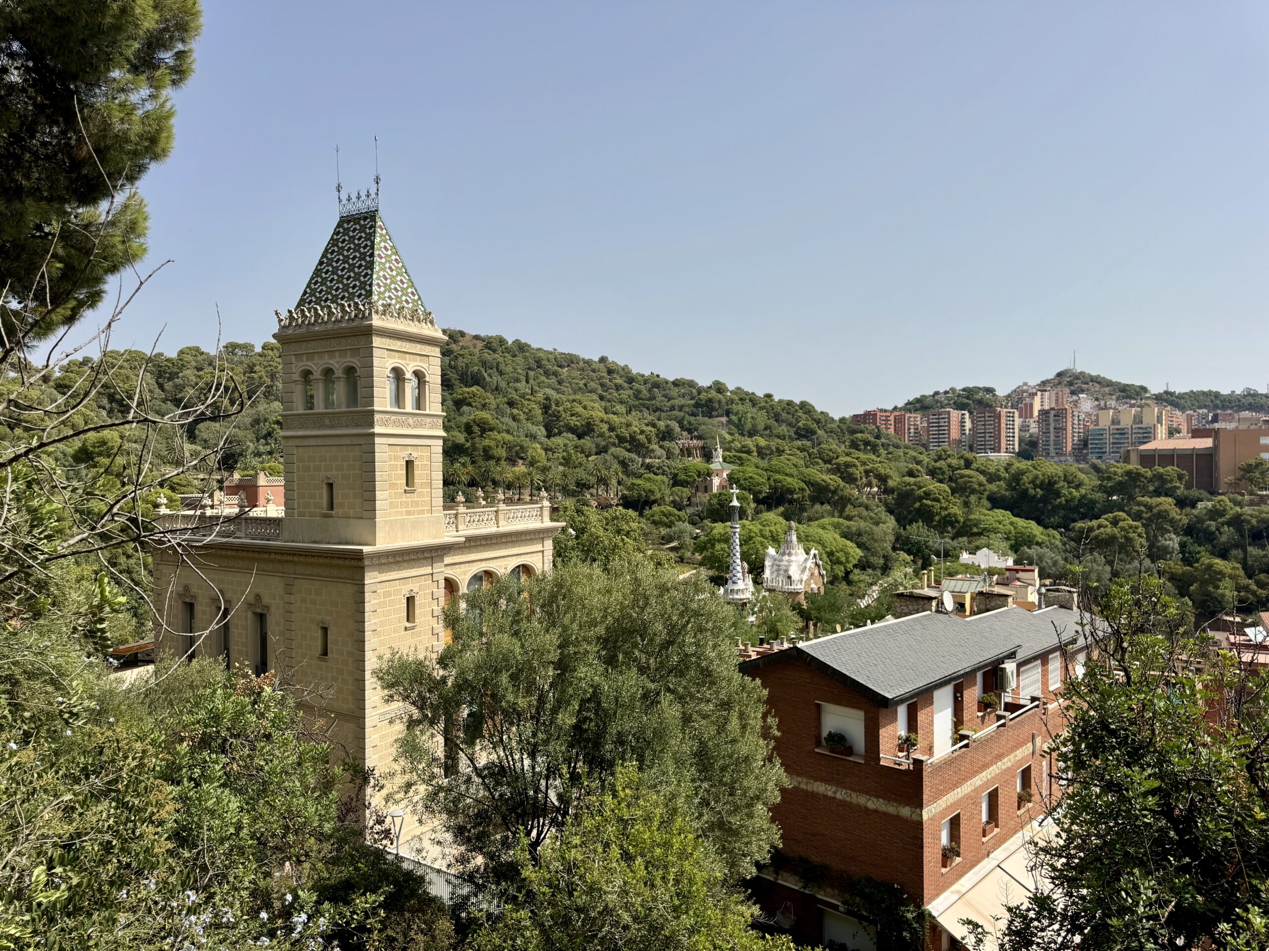 Stone tower with a decorative tiled roof in a green landscape, overlooking a city in the distance.