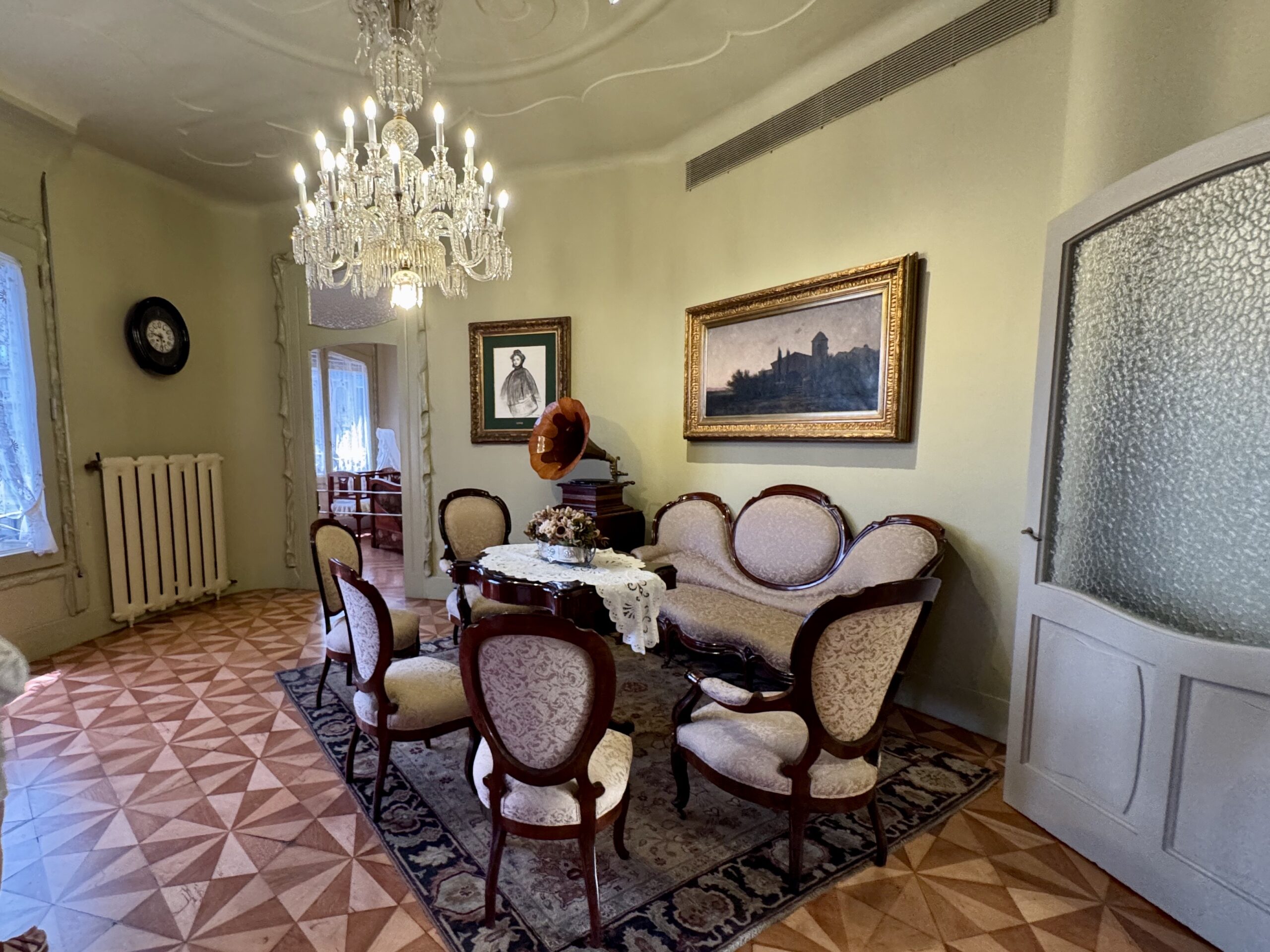 Elegant vintage dining room with a crystal chandelier above a lace-covered table and upholstered chairs around it.