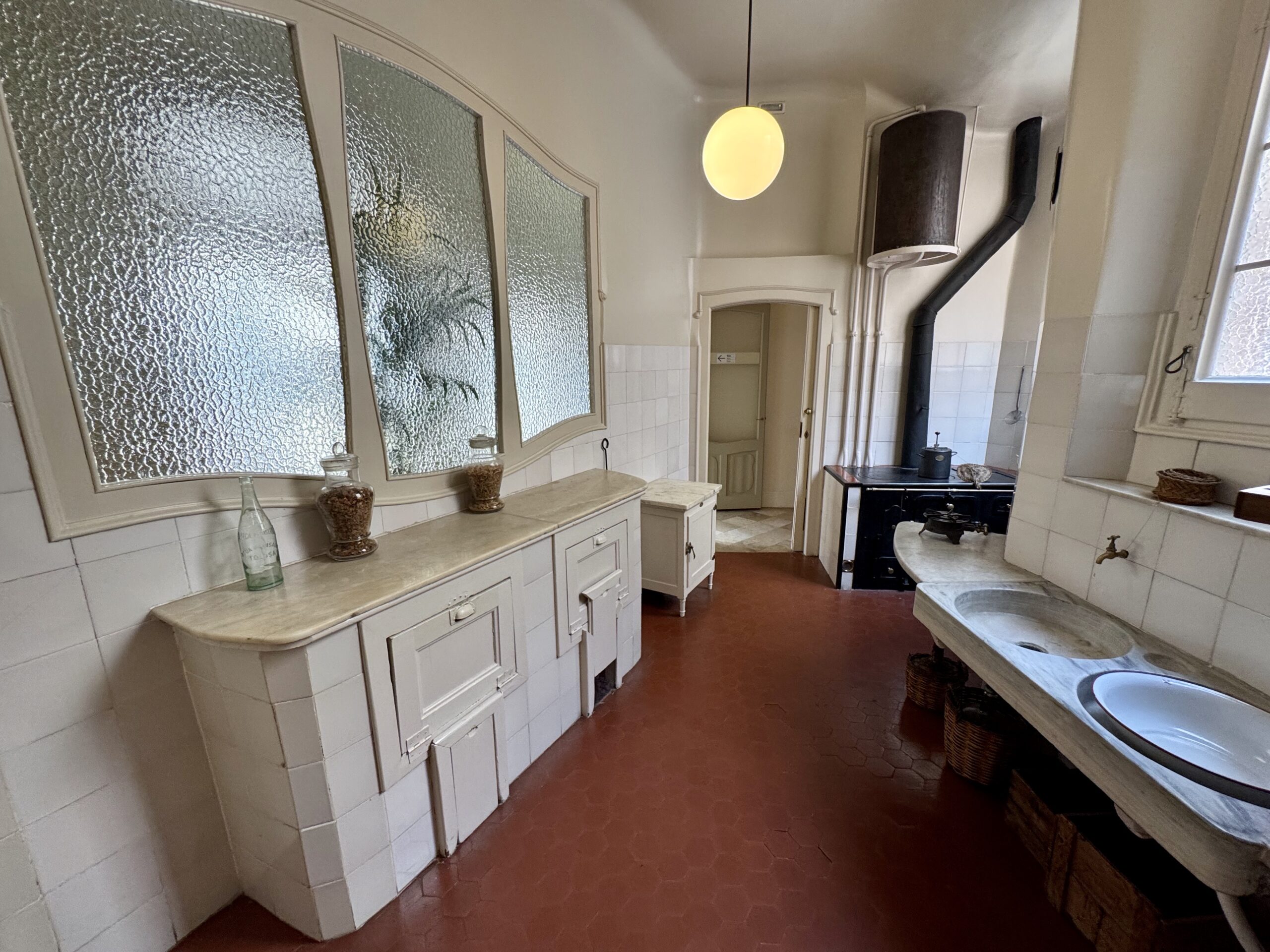 Old-fashioned kitchen with white, frosted-glass cabinets, marble counter, and a black stove against tiled walls.